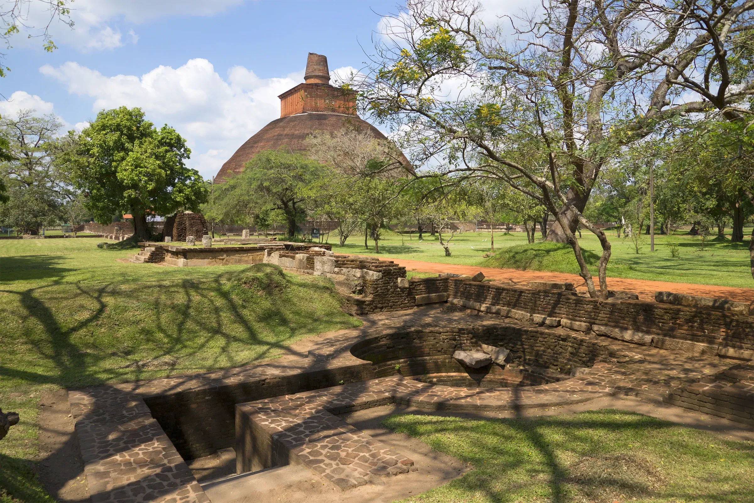 Grassy archaeological park with a brick dagoba and ancient stone ruins at Anuradhapura