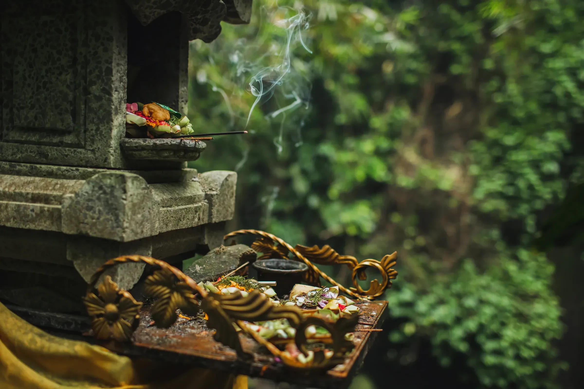 Canang sari offerings and smoking incense on a stone shrine in Bali