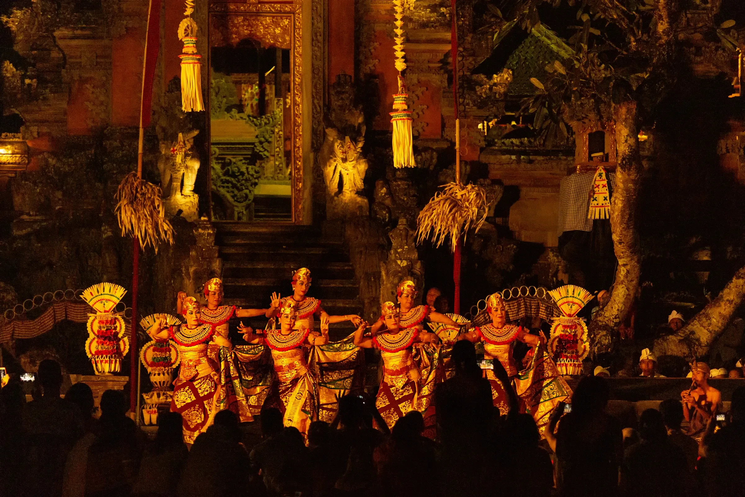 Balinese dancers in gold costumes performing in front of a lit temple at night