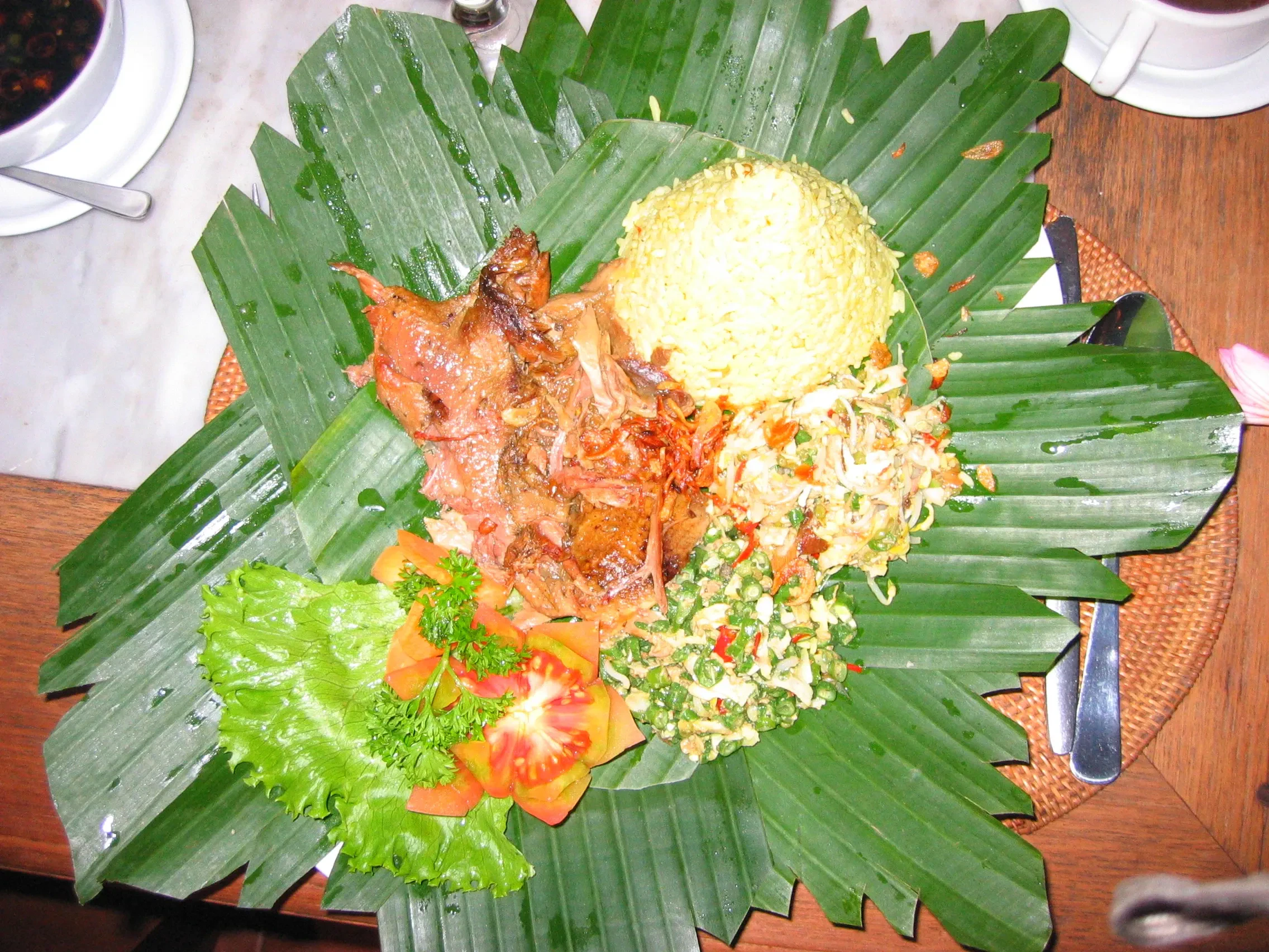Bebek betutu spiced duck served on a banana leaf with rice and vegetables
