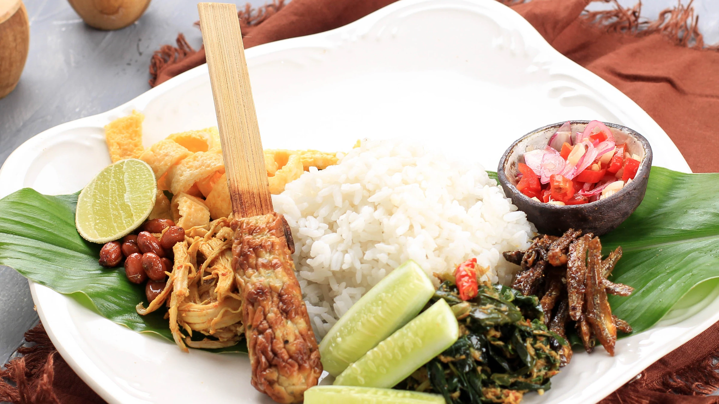 A Balinese nasi campur plate with rice, a sate lilit skewer, vegetables and sambal