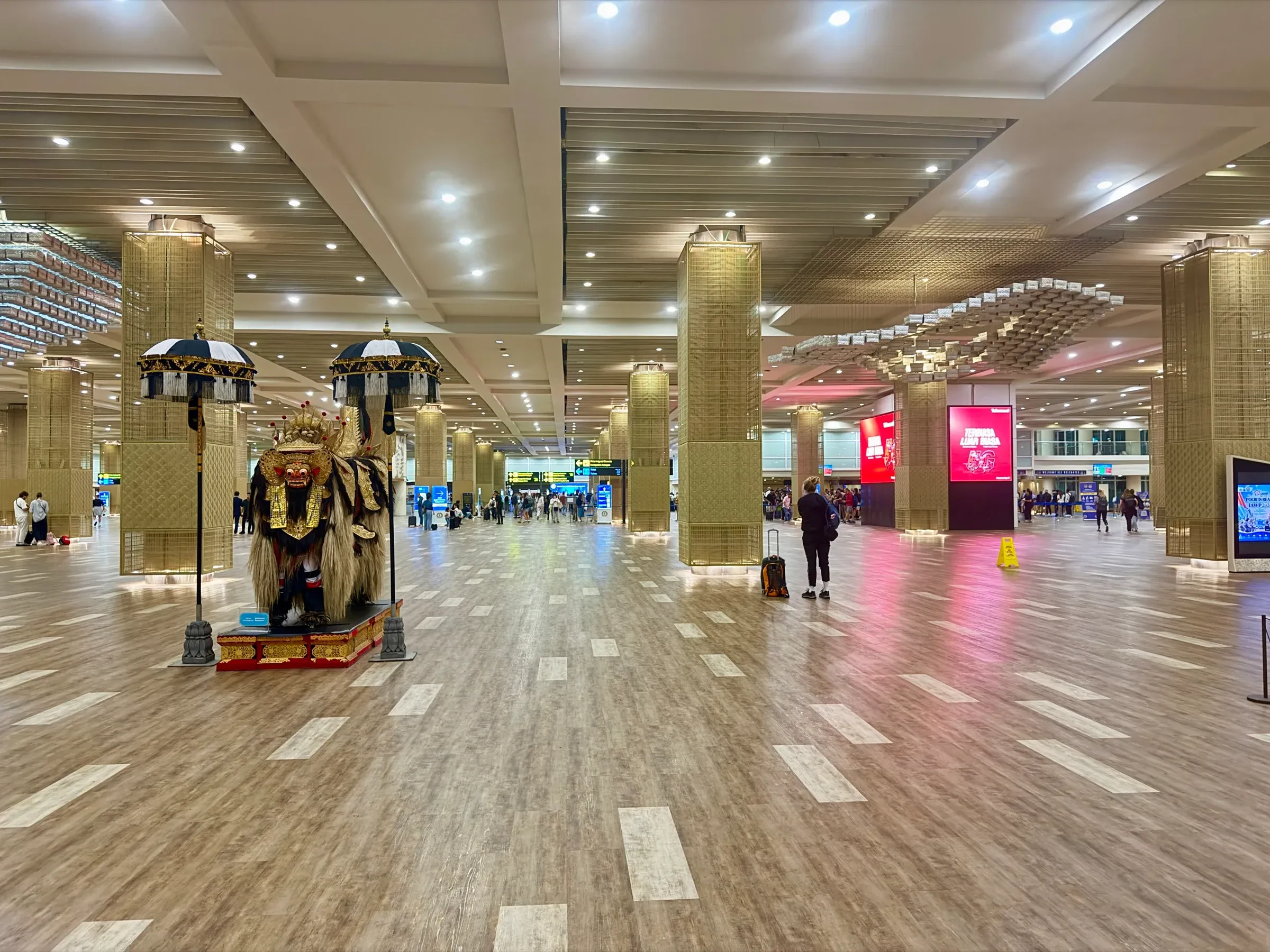 A Balinese statue among brass-coloured pillars in a wide hall of the international terminal at Ngurah Rai airport