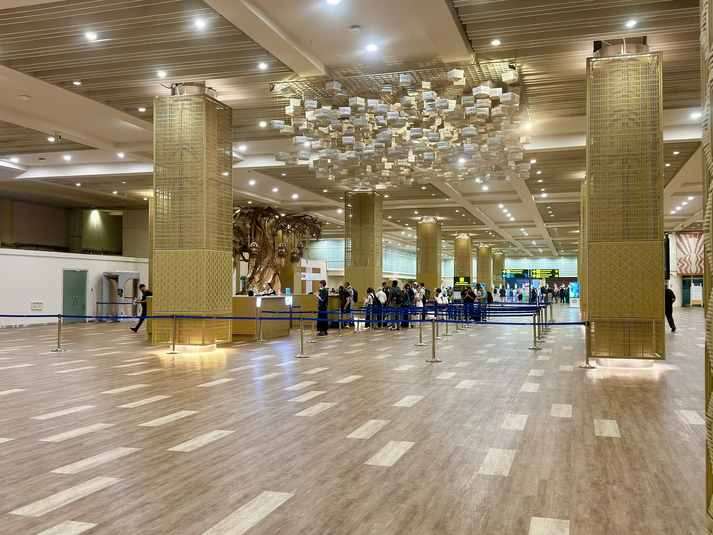 A wide hall with brass-coloured pillars and a chandelier in the international terminal at Ngurah Rai airport