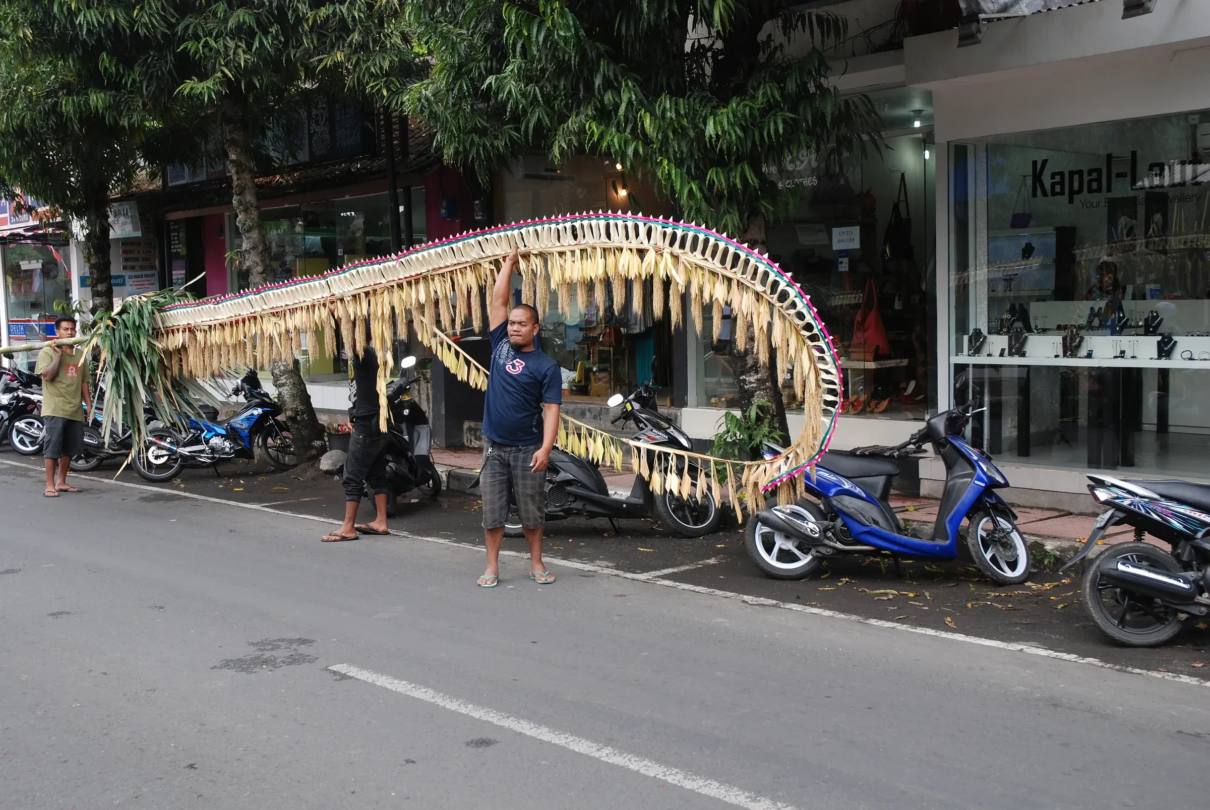 Men raising a tall bamboo penjor beside a street in Ubud during Galungan