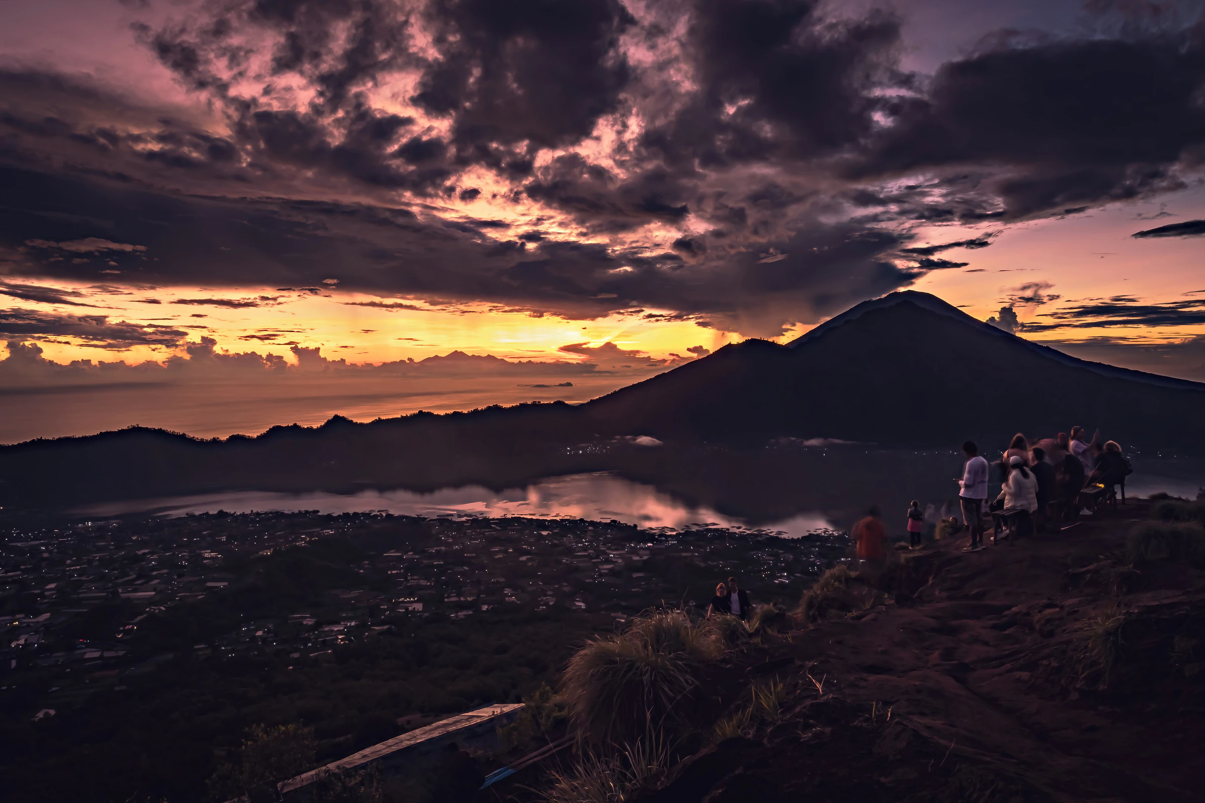 Hikers watching dawn colour the sky over Lake Batur, with the volcano beyond