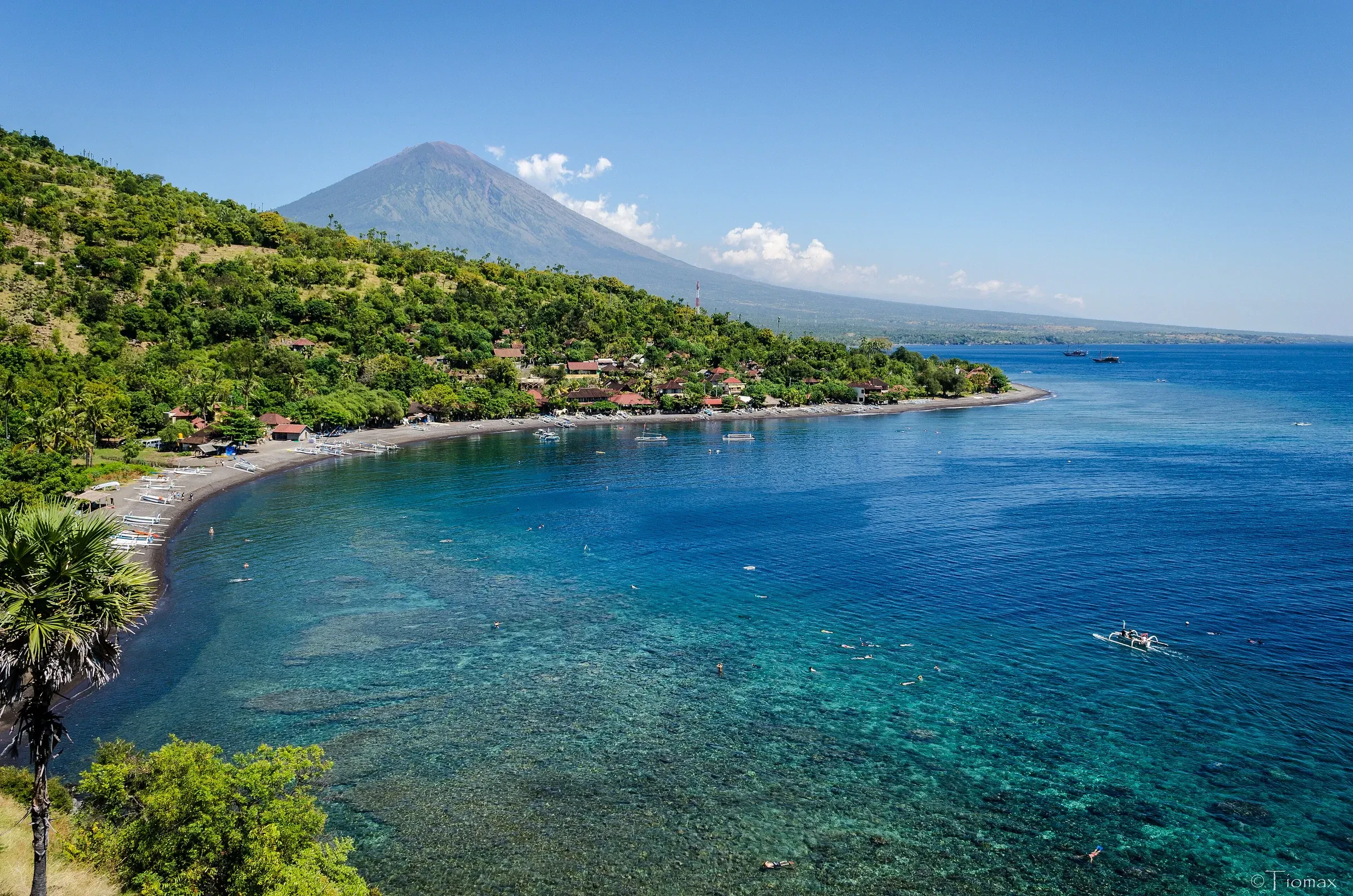 The curved coast and reef at Amed in east Bali, with a volcano rising behind