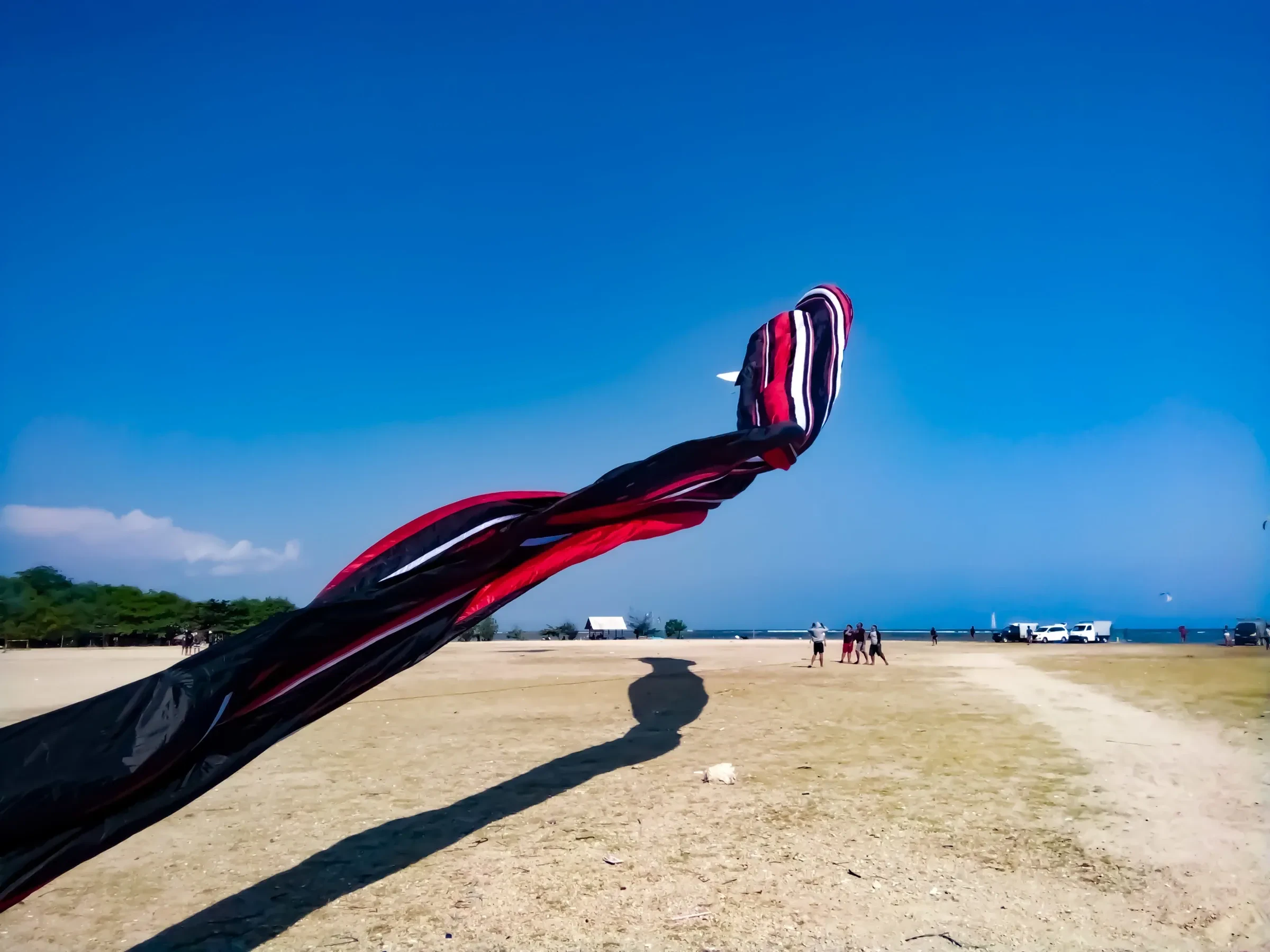 A long kite tail streaming over open ground at Mertasari Beach in Sanur, Bali