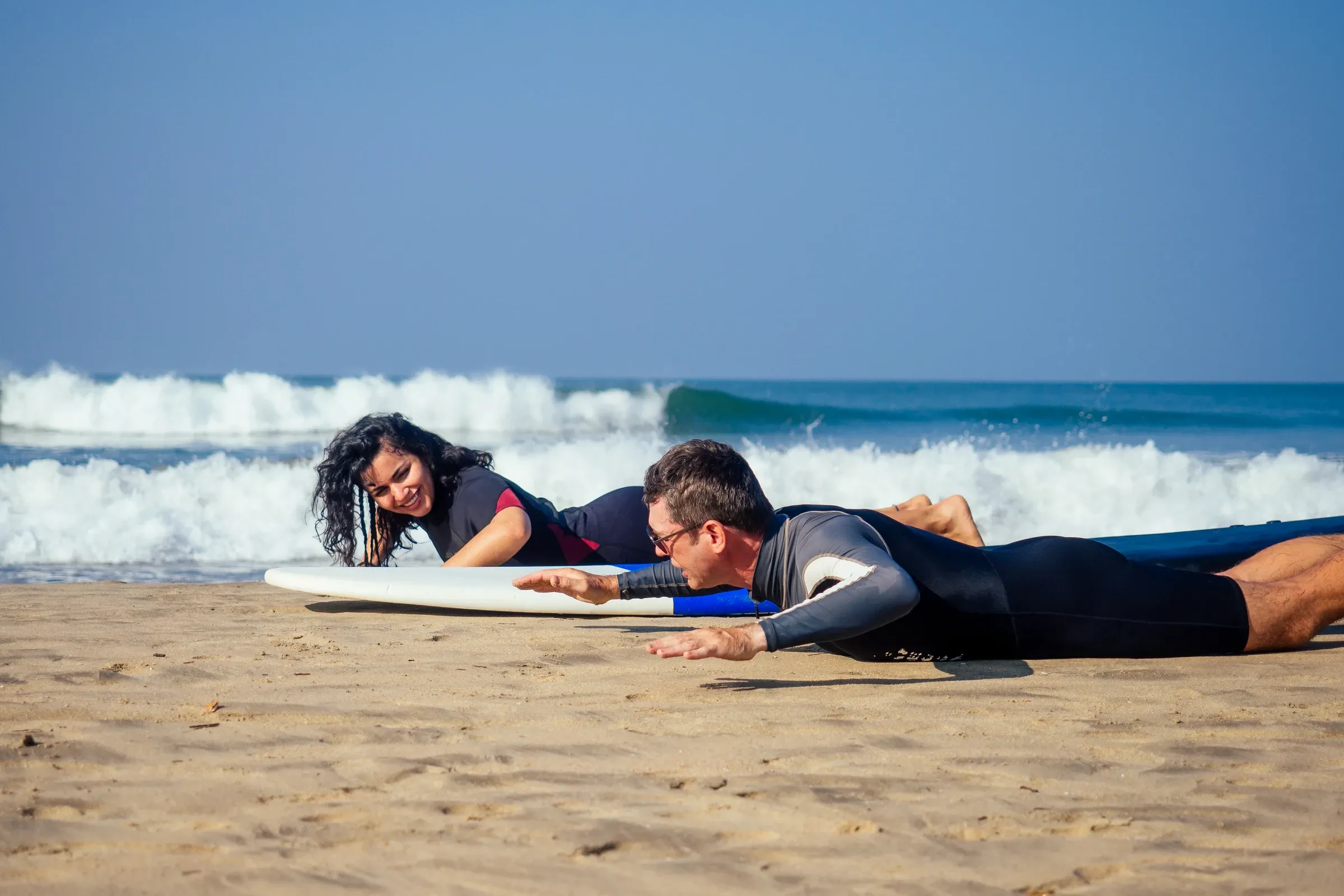 Two beginners practising paddling on surfboards on the sand before a lesson