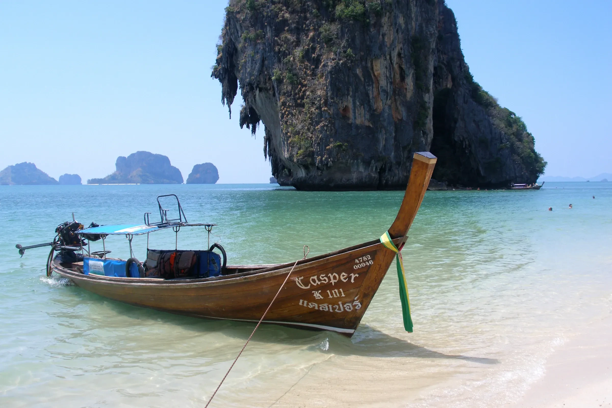 A longtail boat on the shore at Railay, Krabi, with a limestone cliff behind