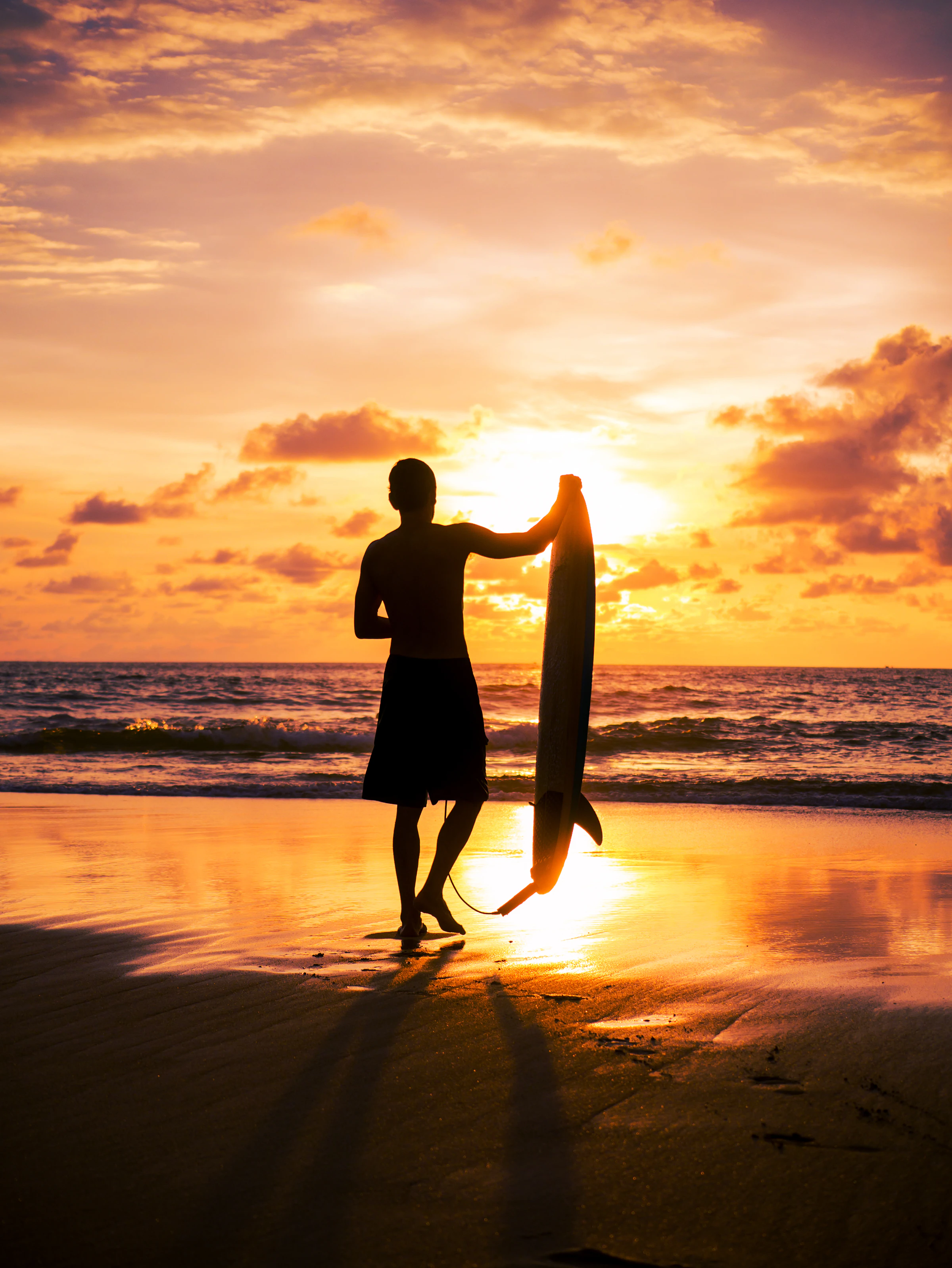 A surfer silhouetted on the beach with his board at sunset in Bali