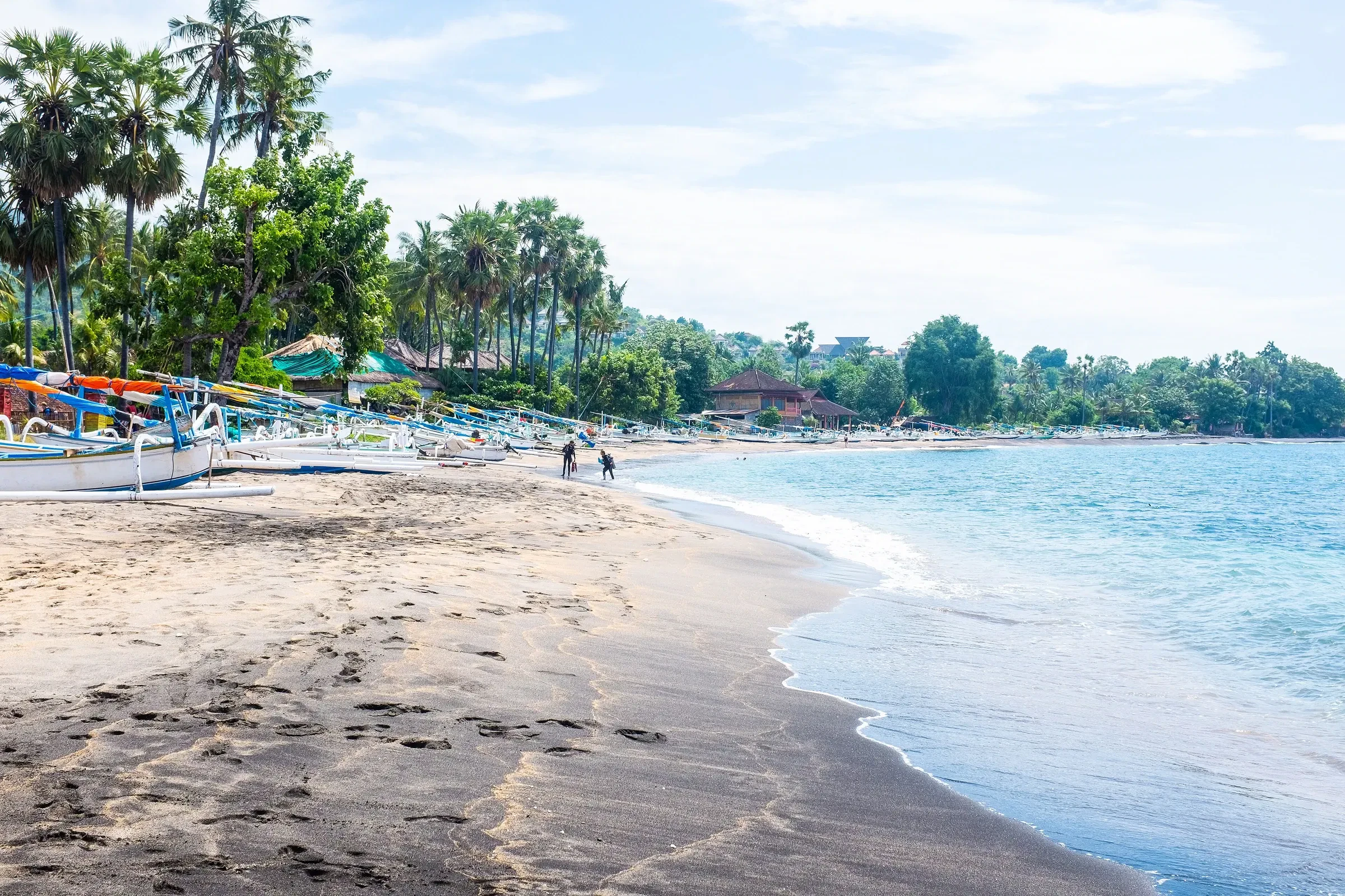 A black sand beach at Amed with colourful outrigger boats under palm trees