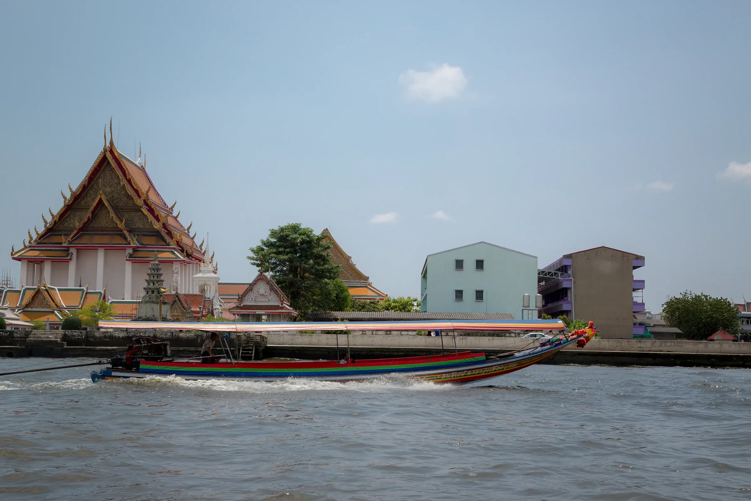 A longtail boat passing a riverside temple on the Chao Phraya in Bangkok