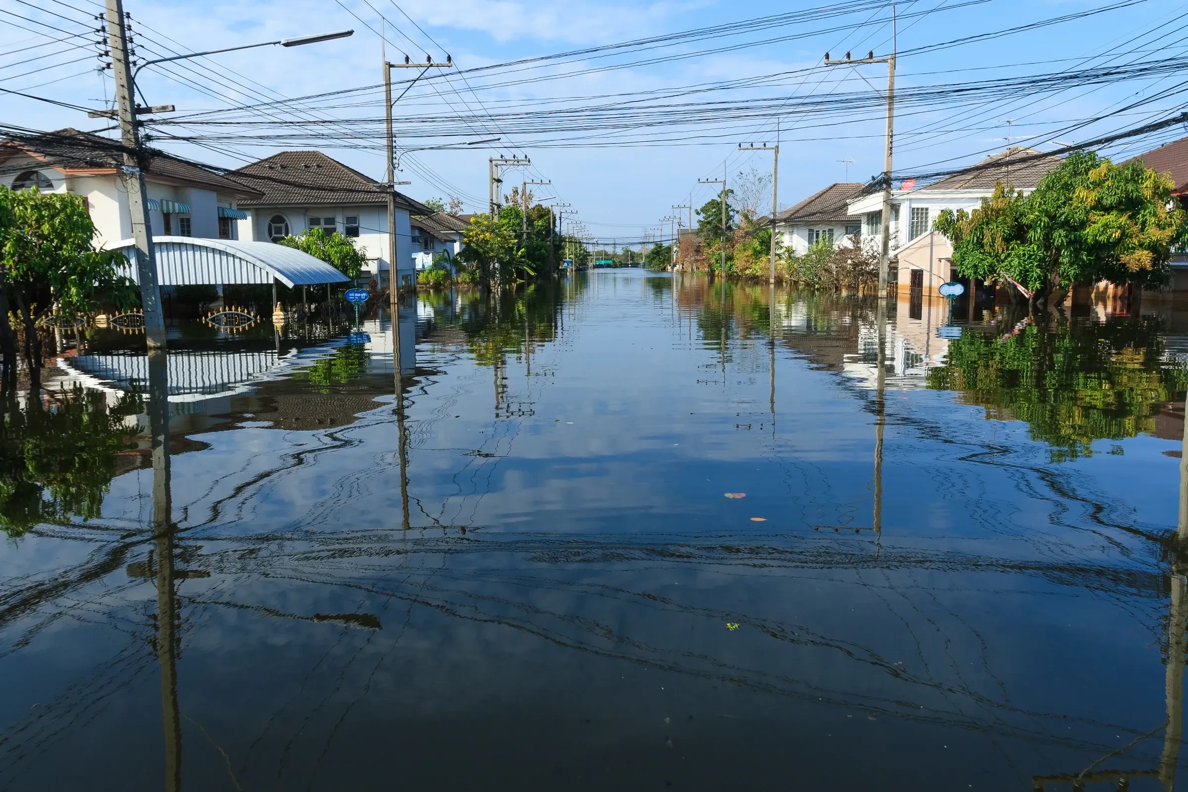 A Bangkok street under floodwater with houses and power lines on both sides