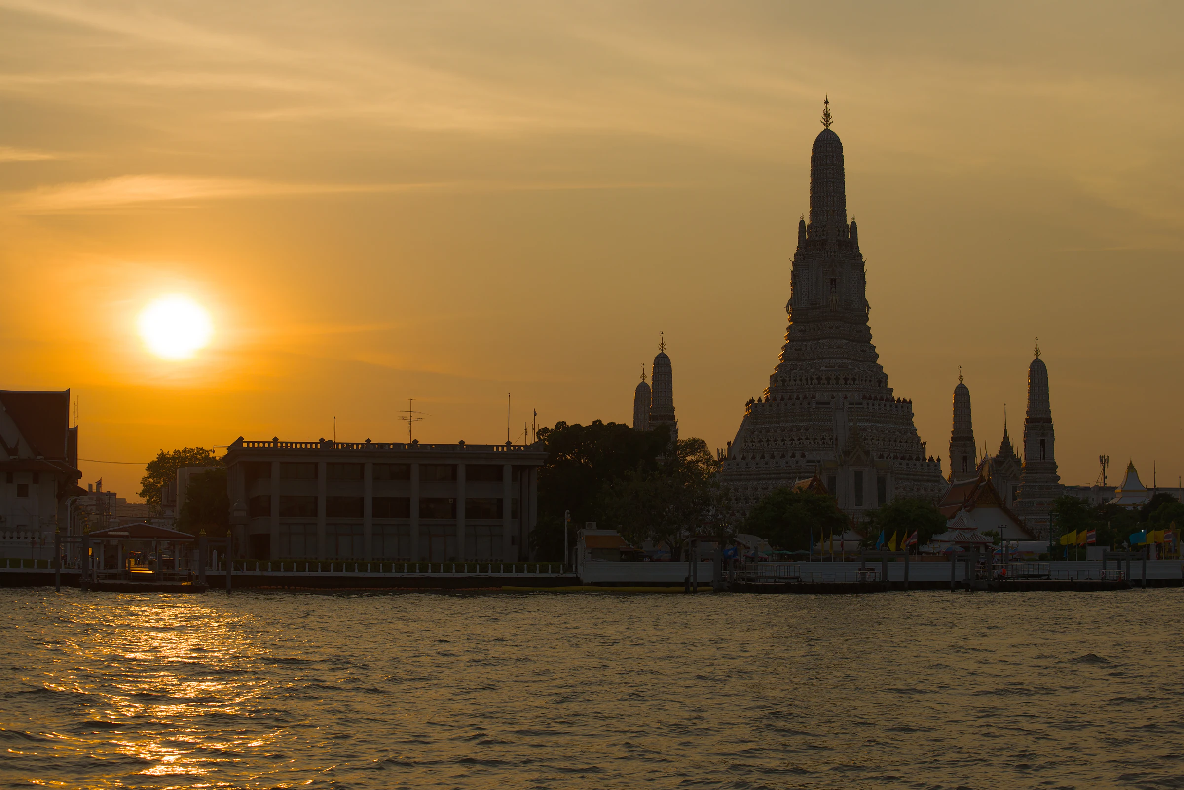 Wat Arun silhouetted against the setting sun across the Chao Phraya River