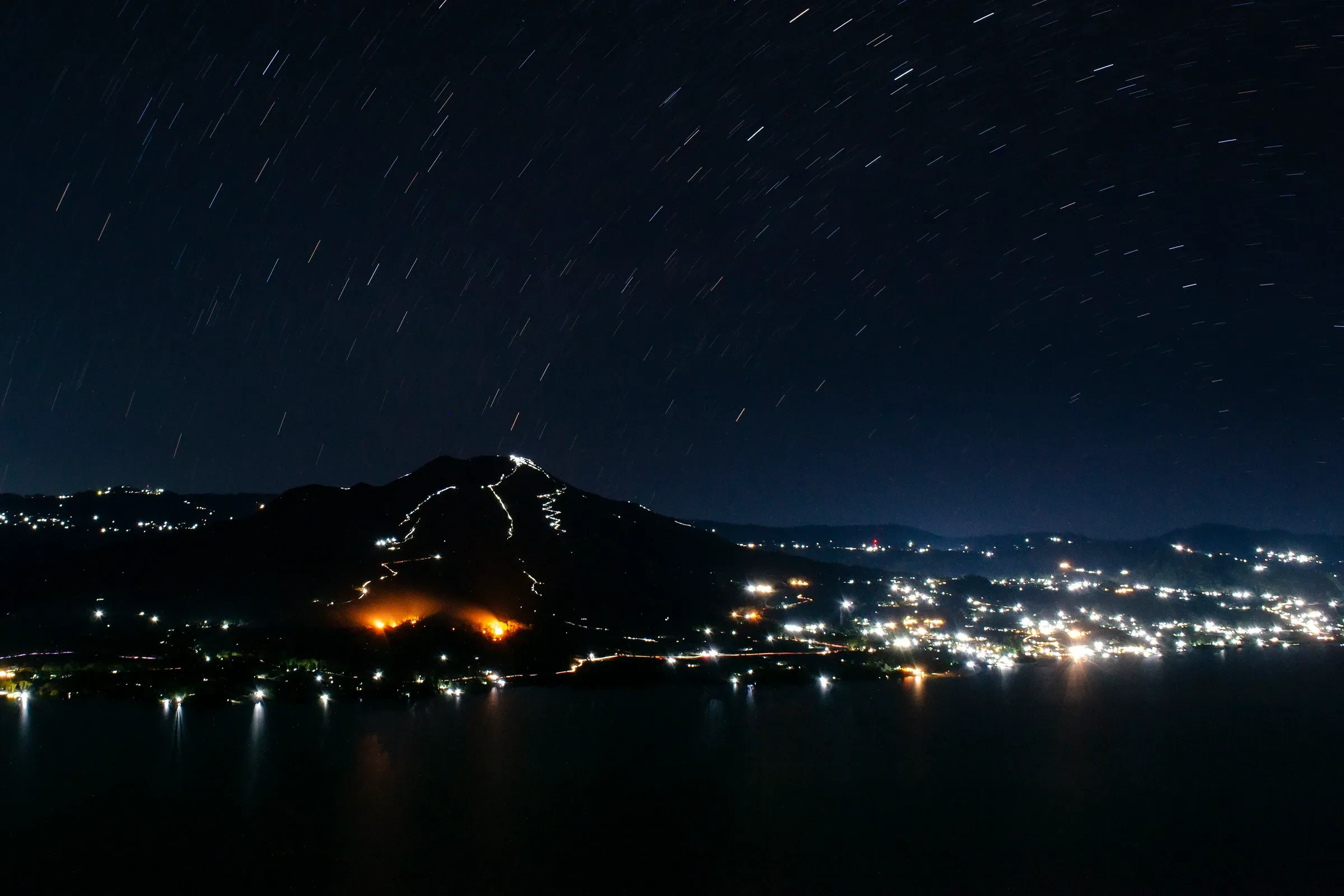Head torch lights zigzagging up Mount Batur's slope in the dark, with the lakeside villages glowing below.