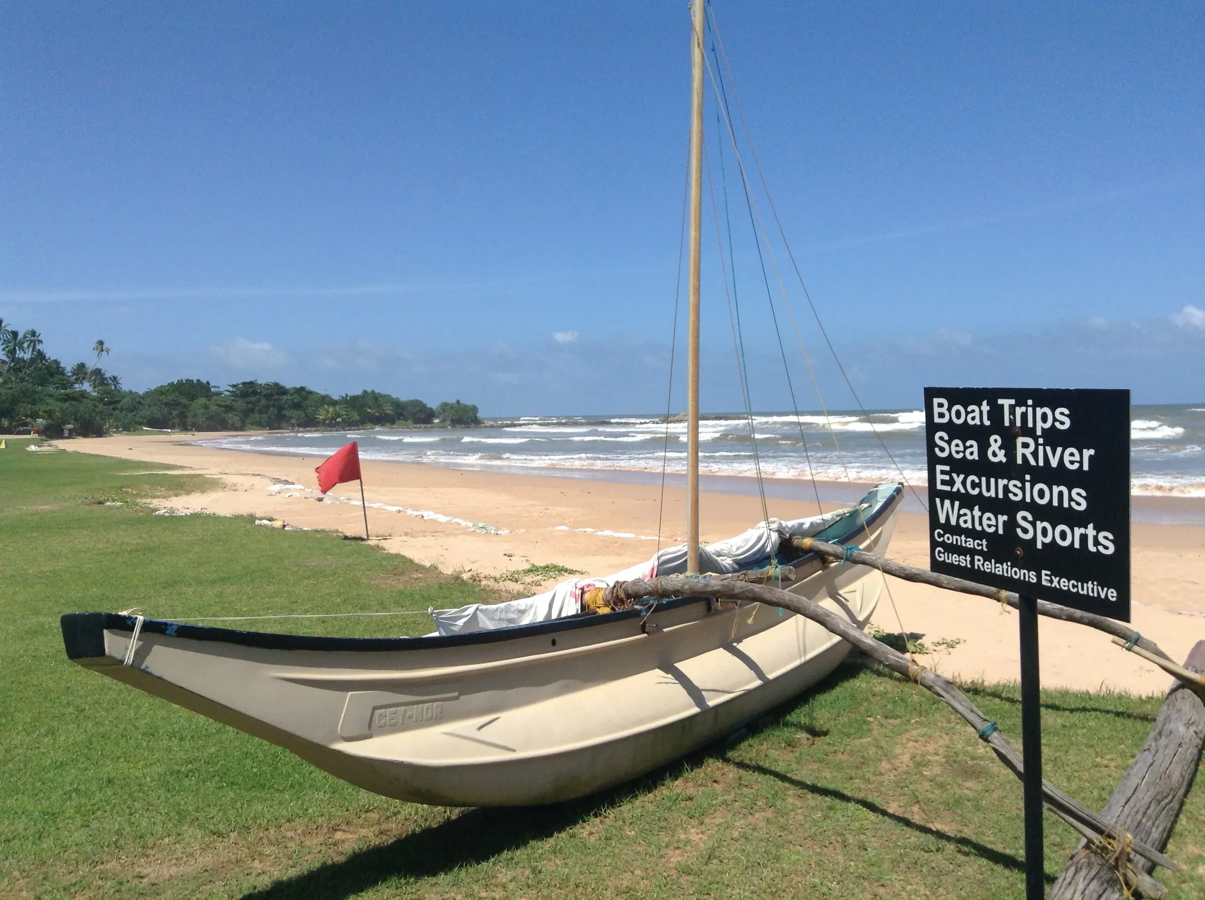 A boat on the sand at Bentota beach beside a sign for boat trips, river excursions and water sports