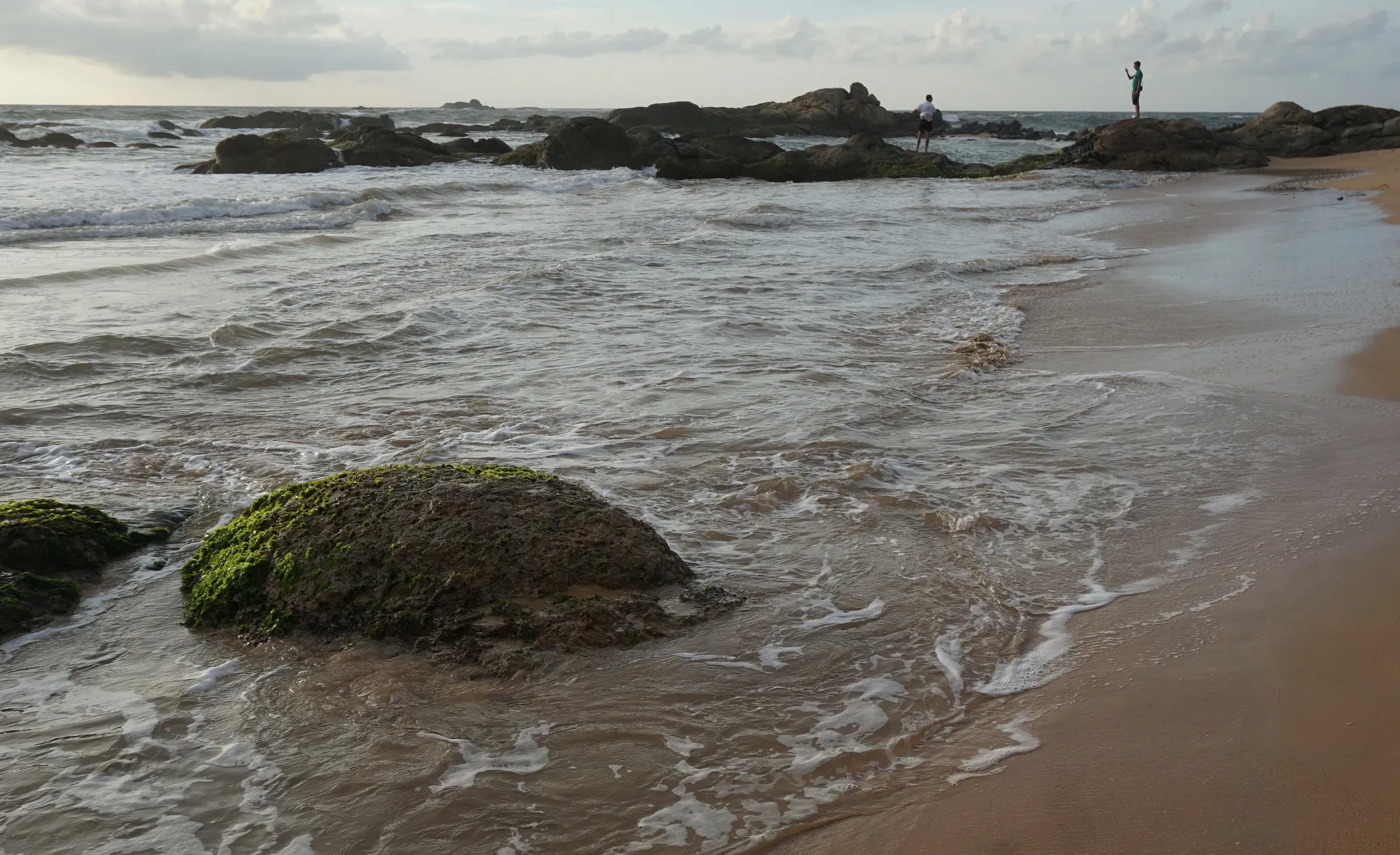 Waves washing over a rocky stretch of Bentota beach with a distant figure on the rocks