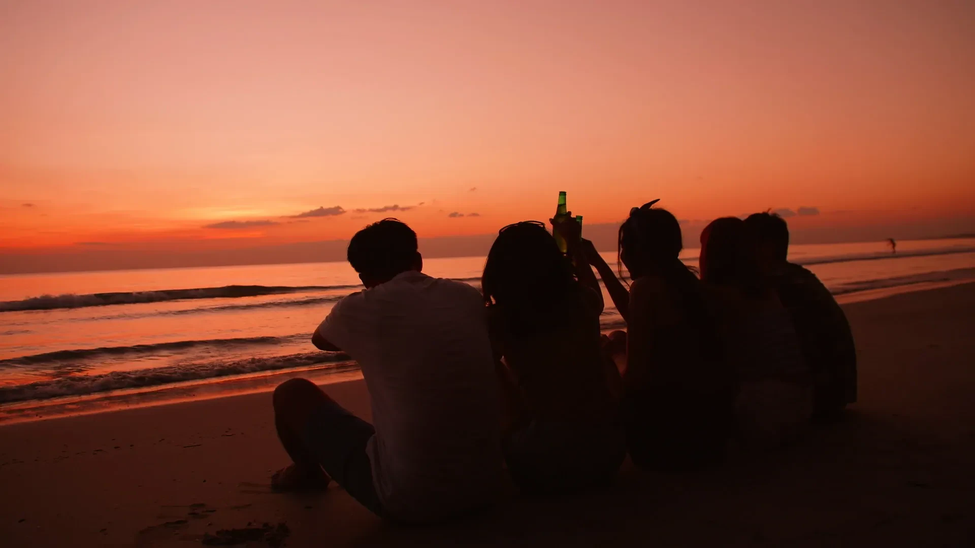 Silhouettes of friends sitting together on a beach at sunset with drinks