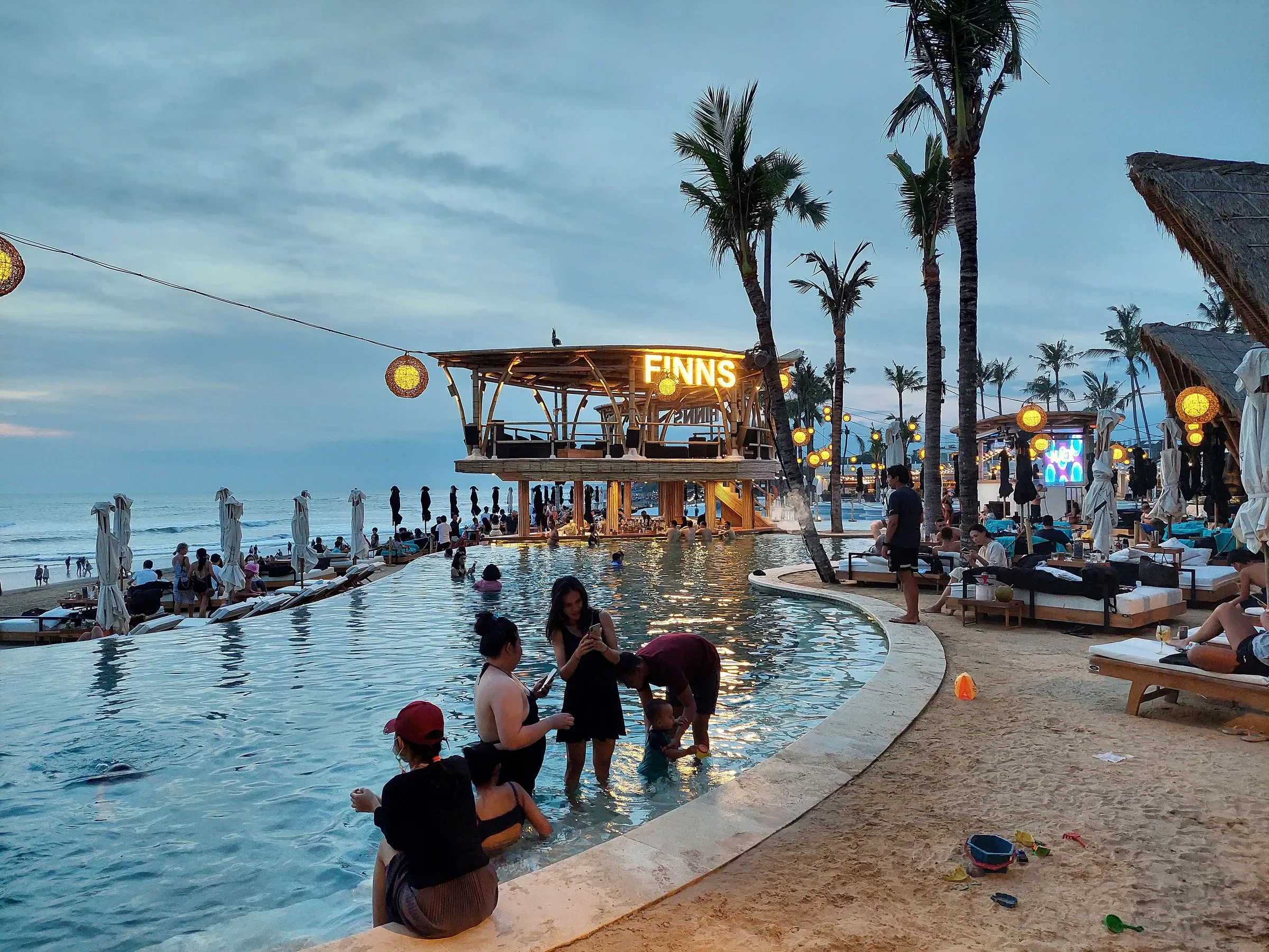 A beach club with an infinity pool and loungers on the Canggu coast at dusk