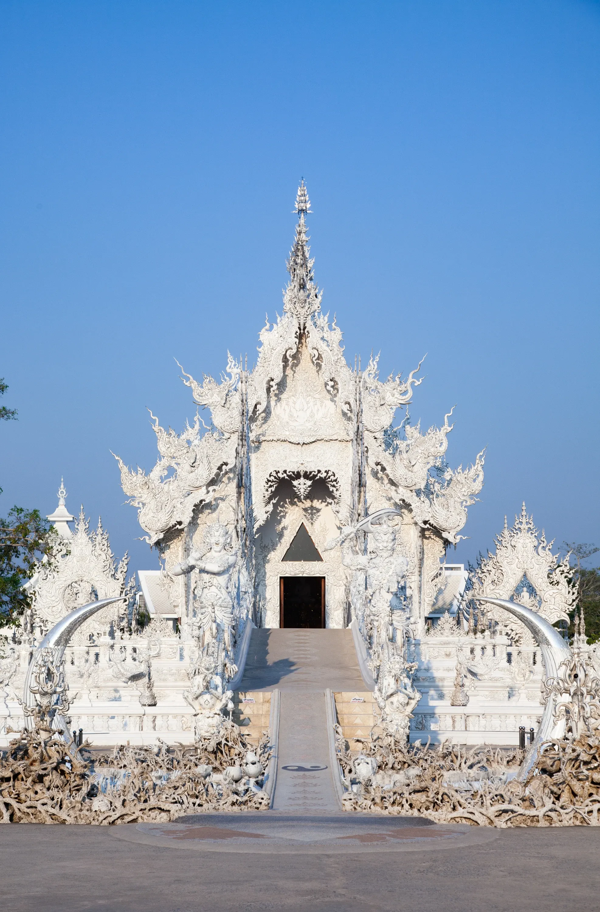 The white carved facade of Wat Rong Khun, the White Temple, at the end of its bridge in Chiang Rai