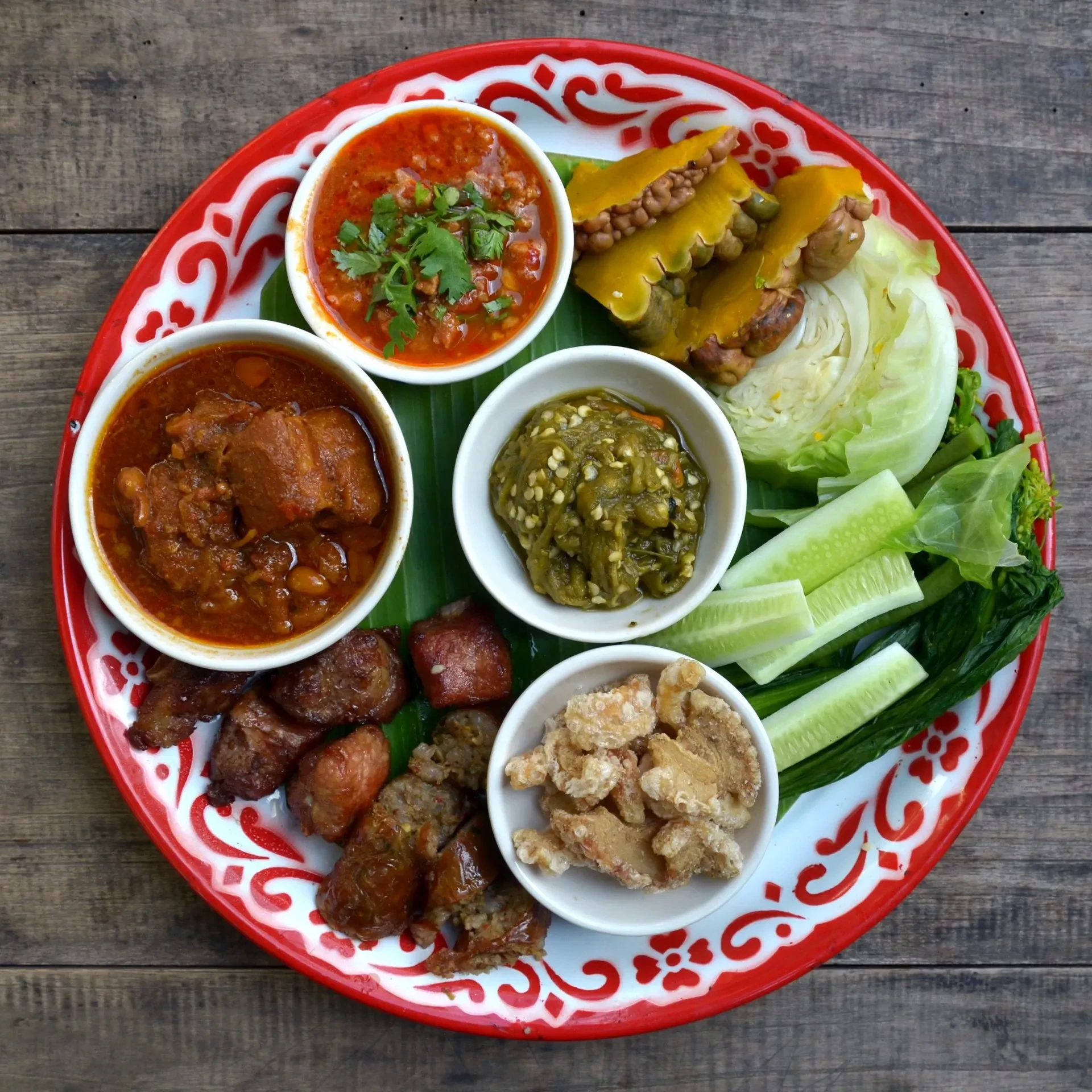 A red enamel platter of northern Thai starters with sai ua sausage and nam prik dips