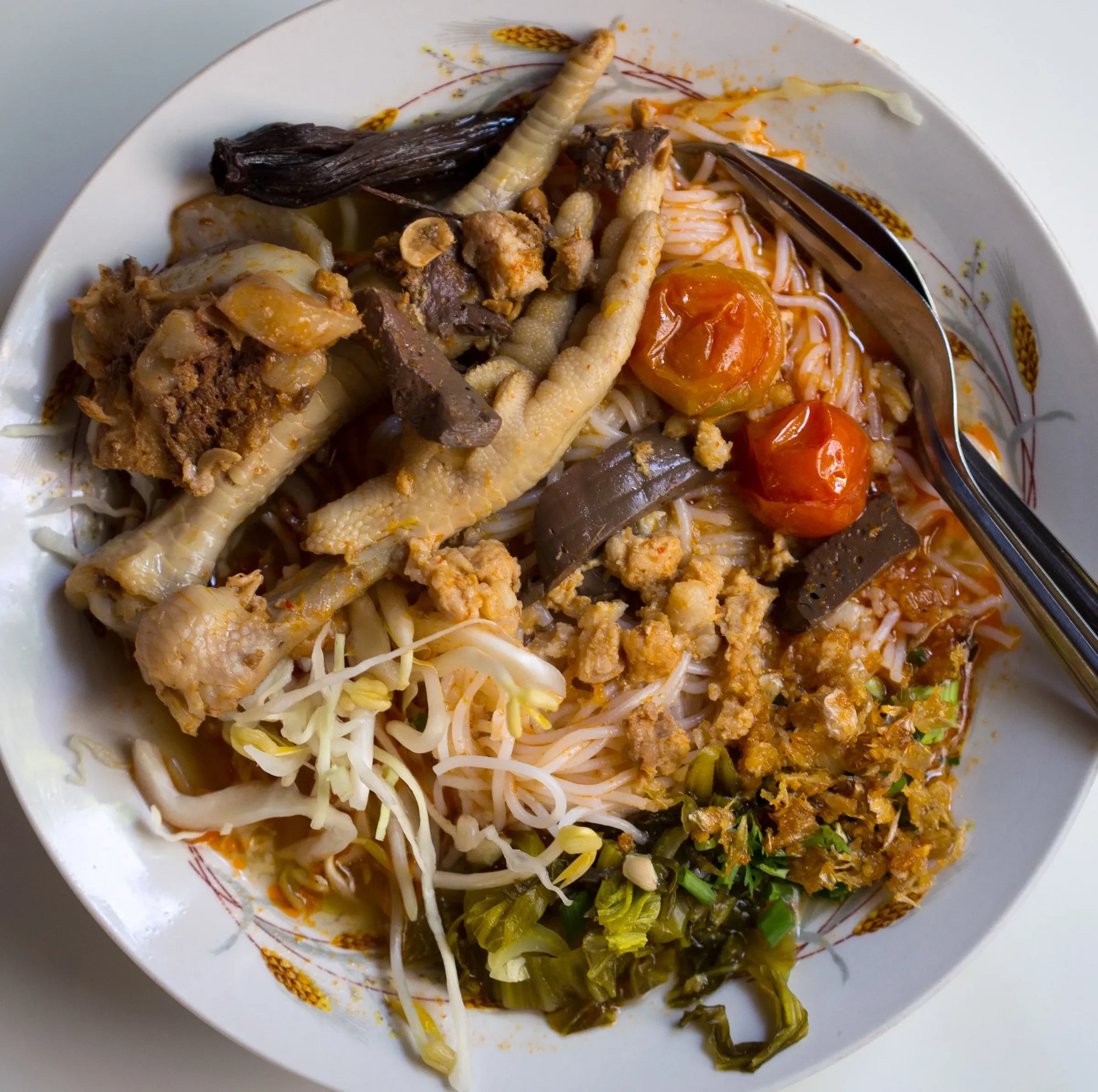 A bowl of khanom jeen nam ngiao with rice noodles, tomatoes and pickled greens