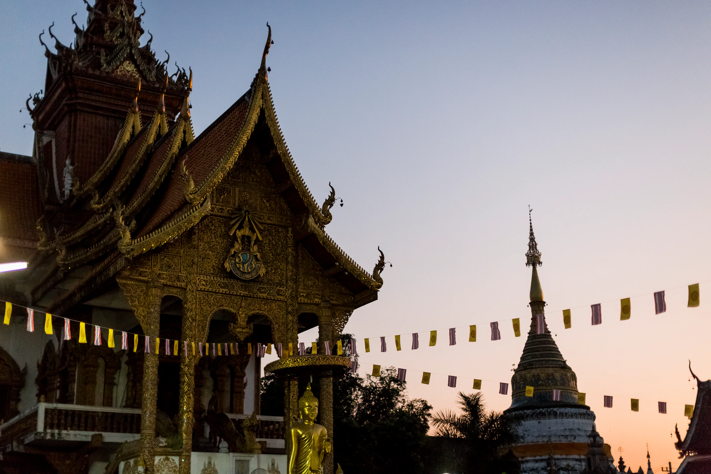 Temple roofs and a chedi strung with prayer flags at dusk in Chiang Mai