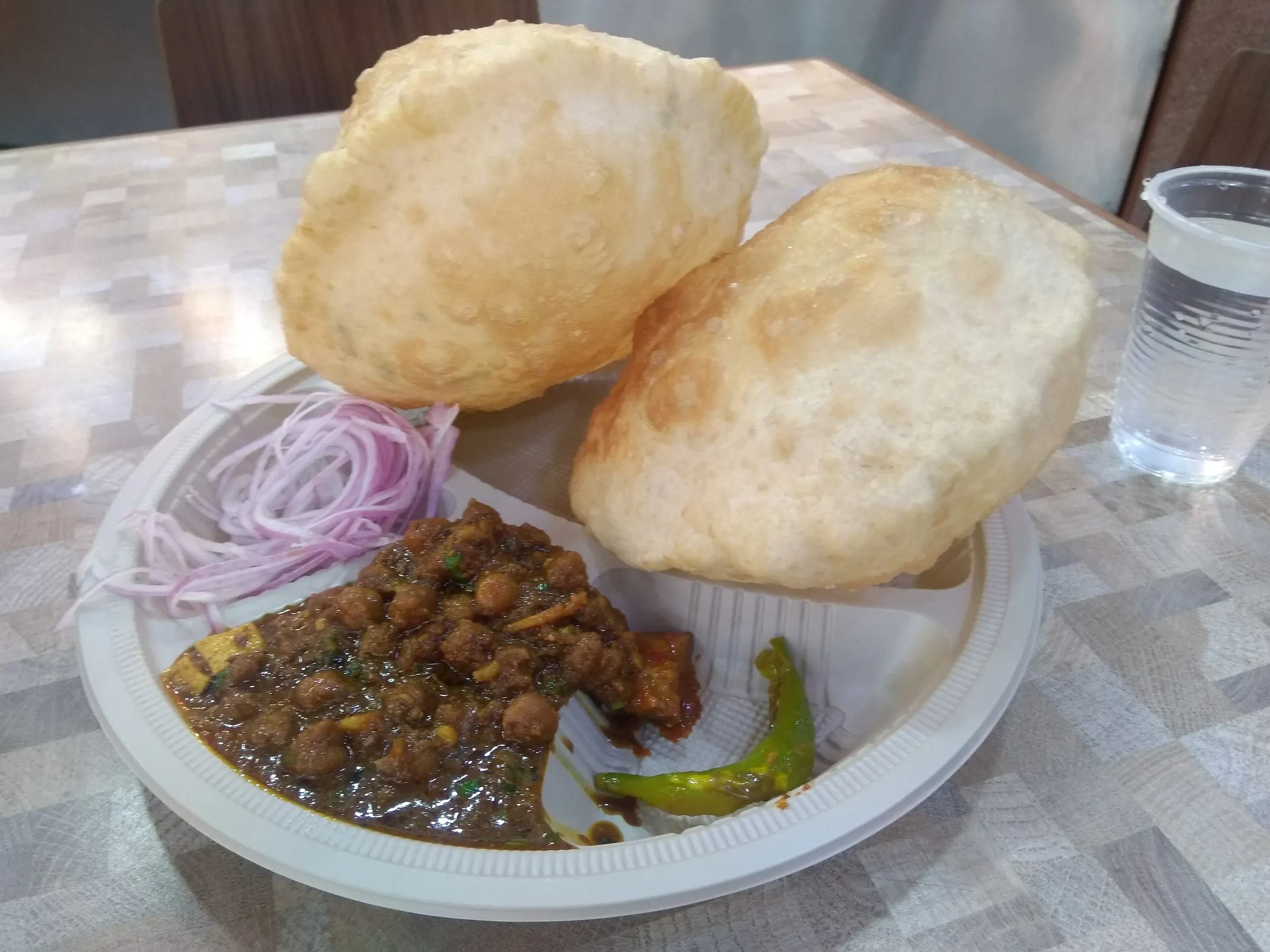 Chole bhature on a disposable plate with onions and green chilli in New Delhi