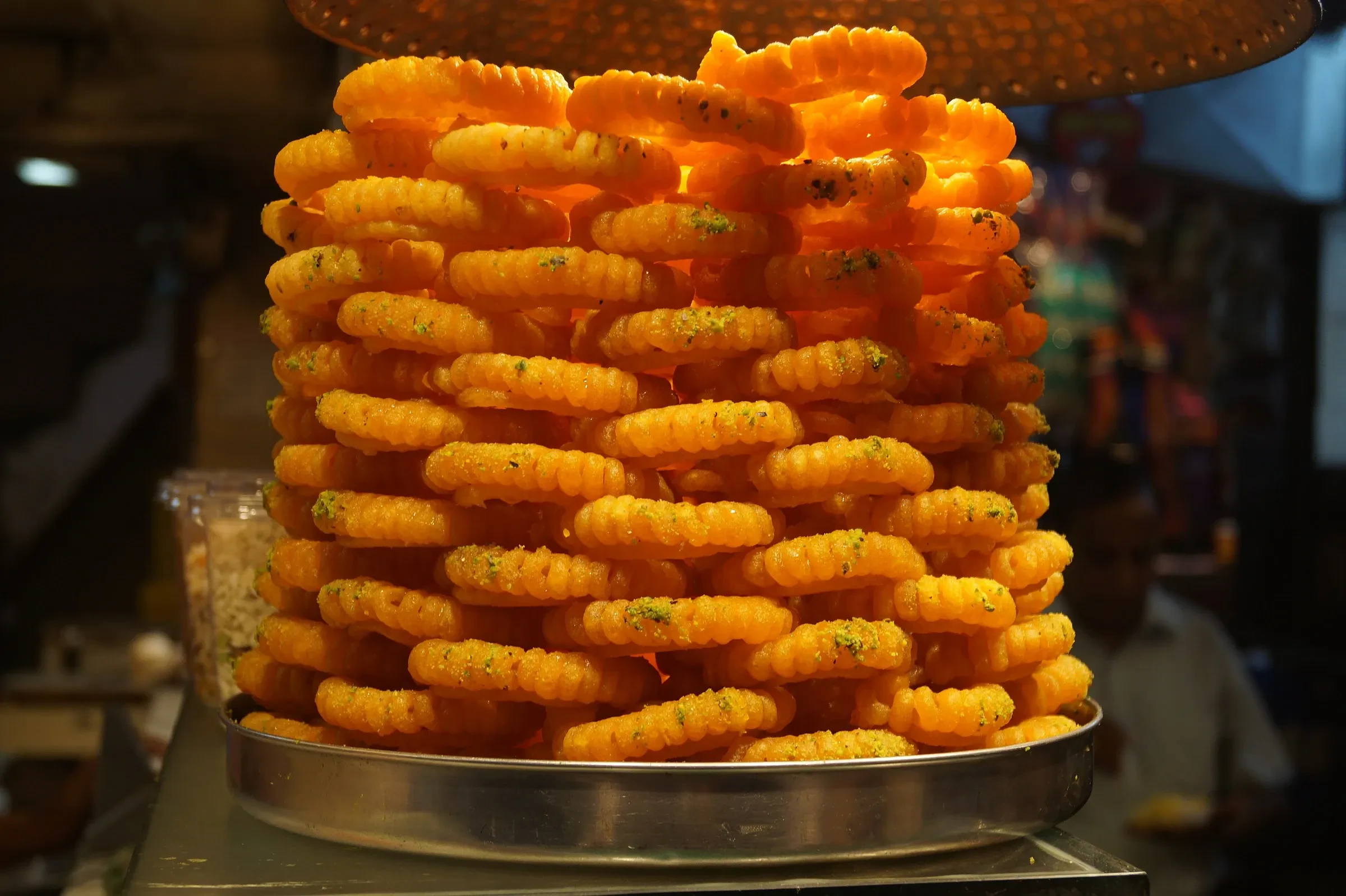 A tall stack of orange jalebi spirals at a sweet stall in Chandni Chowk