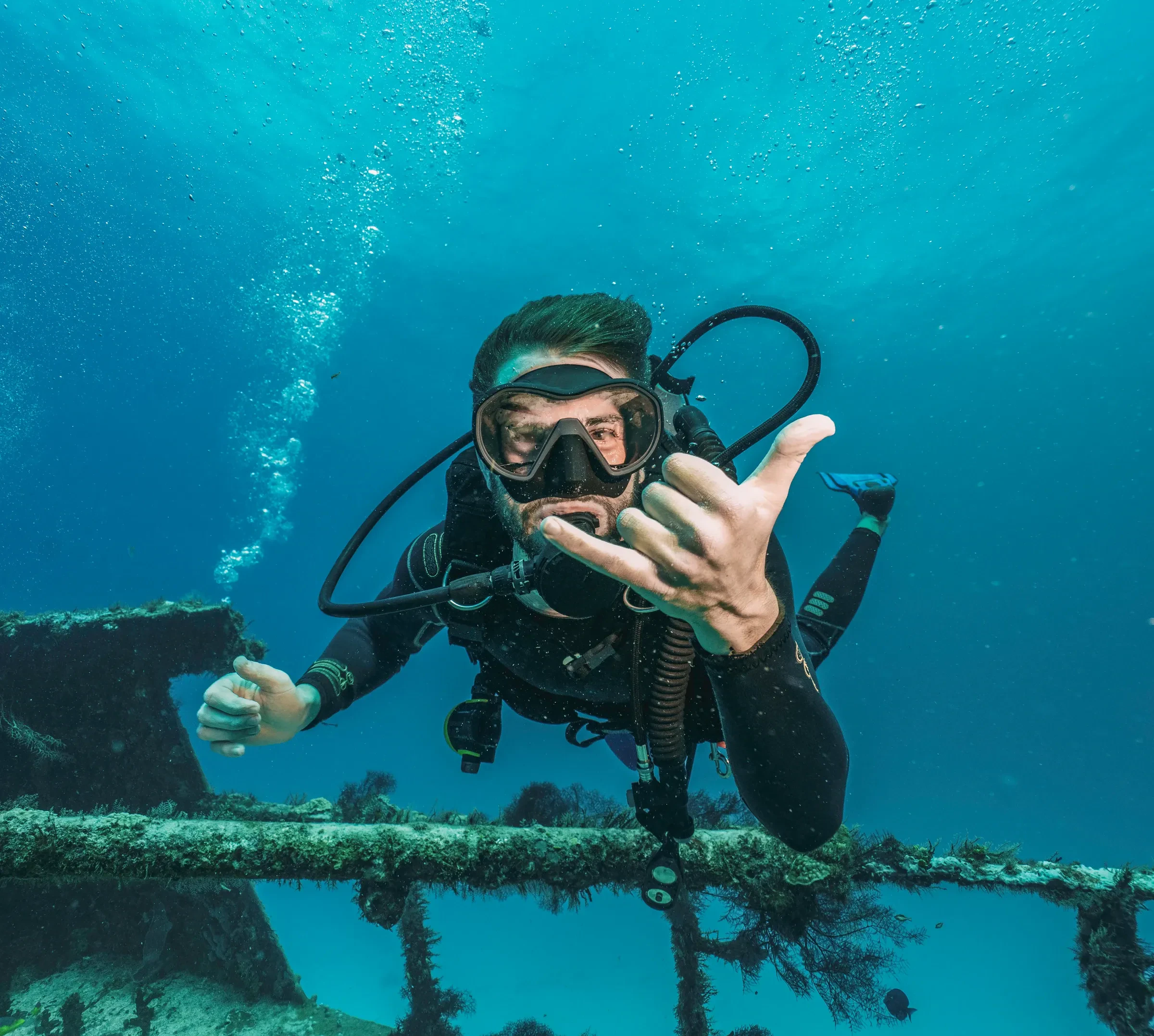A scuba diver in a mask and wetsuit making a hand sign underwater