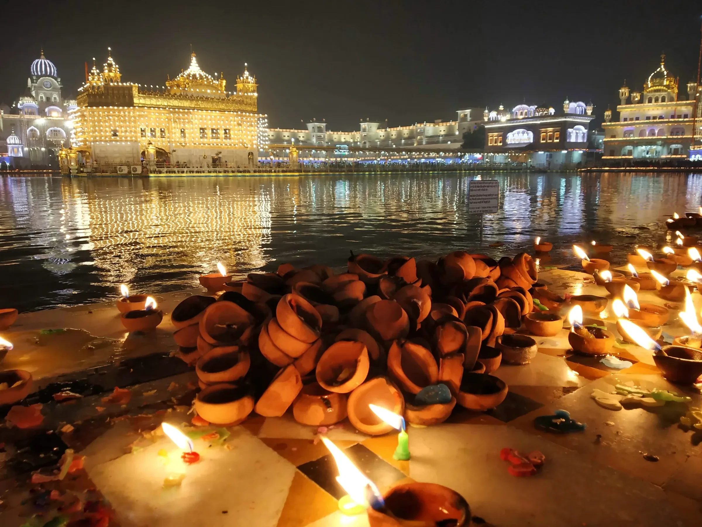 The Golden Temple in Amritsar glowing at night, with rows of clay lamps lit at the water's edge during Diwali