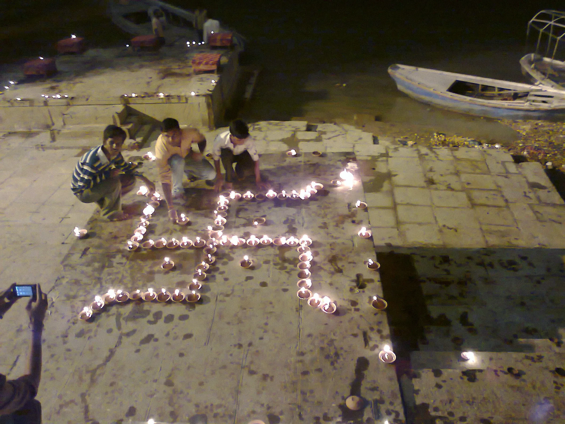 Small clay lamps arranged in a swastik pattern on a Varanasi ghat beside moored boats