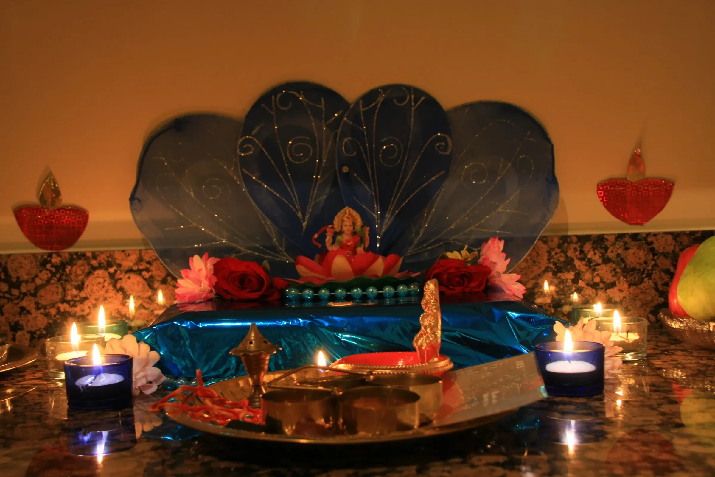 A home shrine with a Lakshmi figure, flowers, candles and diyas set up for Diwali puja