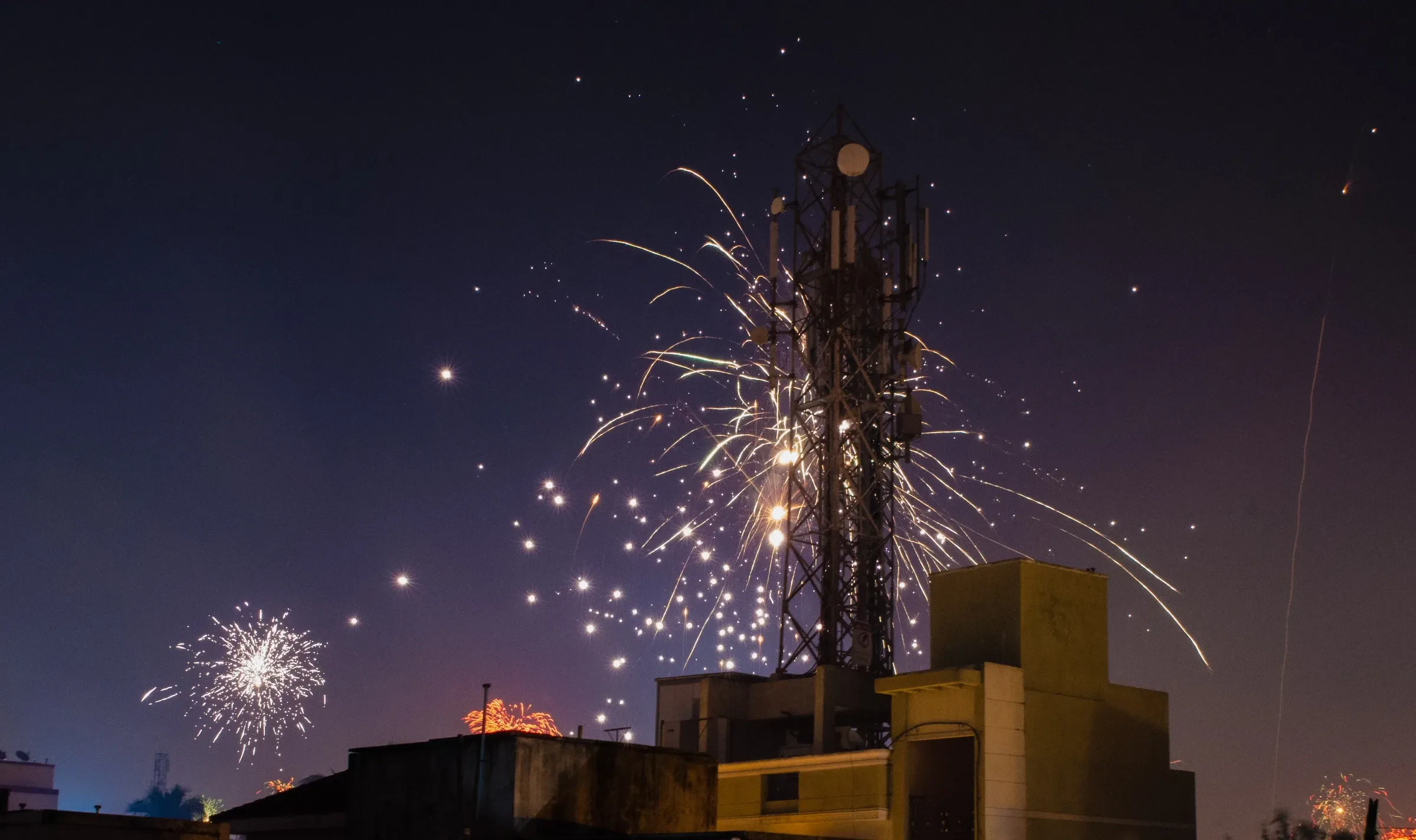 Fireworks bursting over rooftops and a phone tower on Diwali night in India