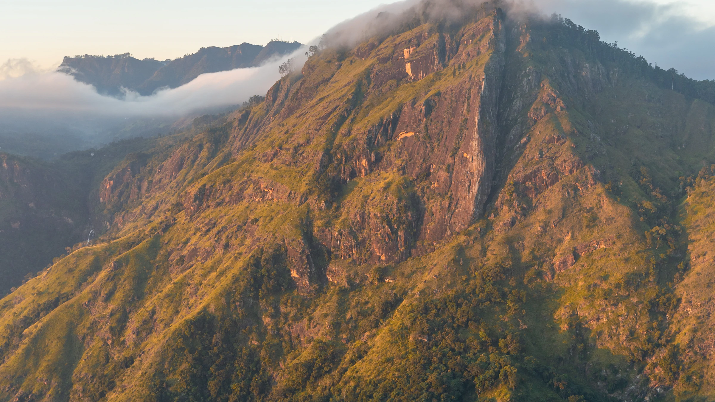 Steep green slopes near Ella lit by low early sun, with cloud lying in the valley