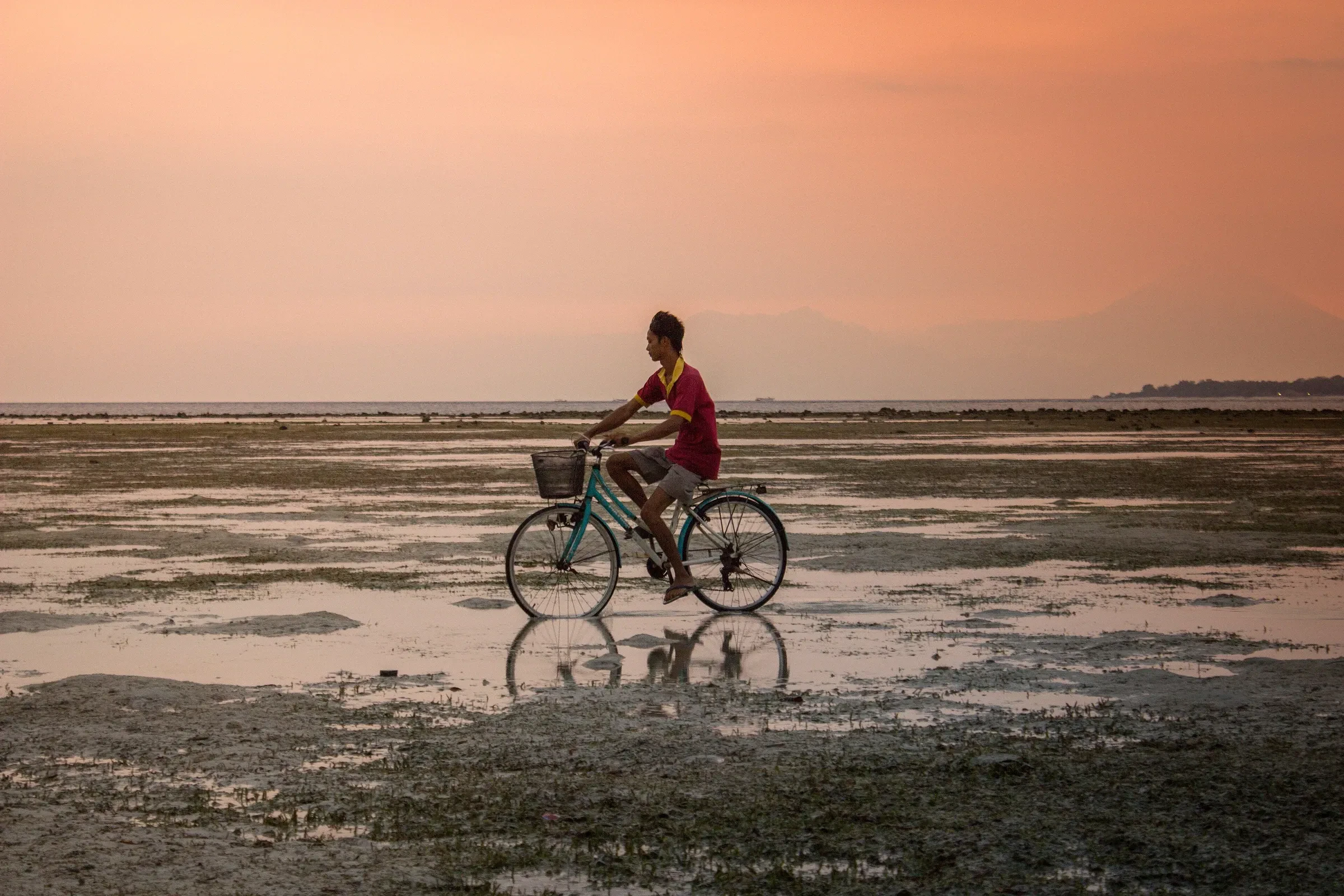A cyclist riding across the exposed tidal flat on Gili Air at sunset.
