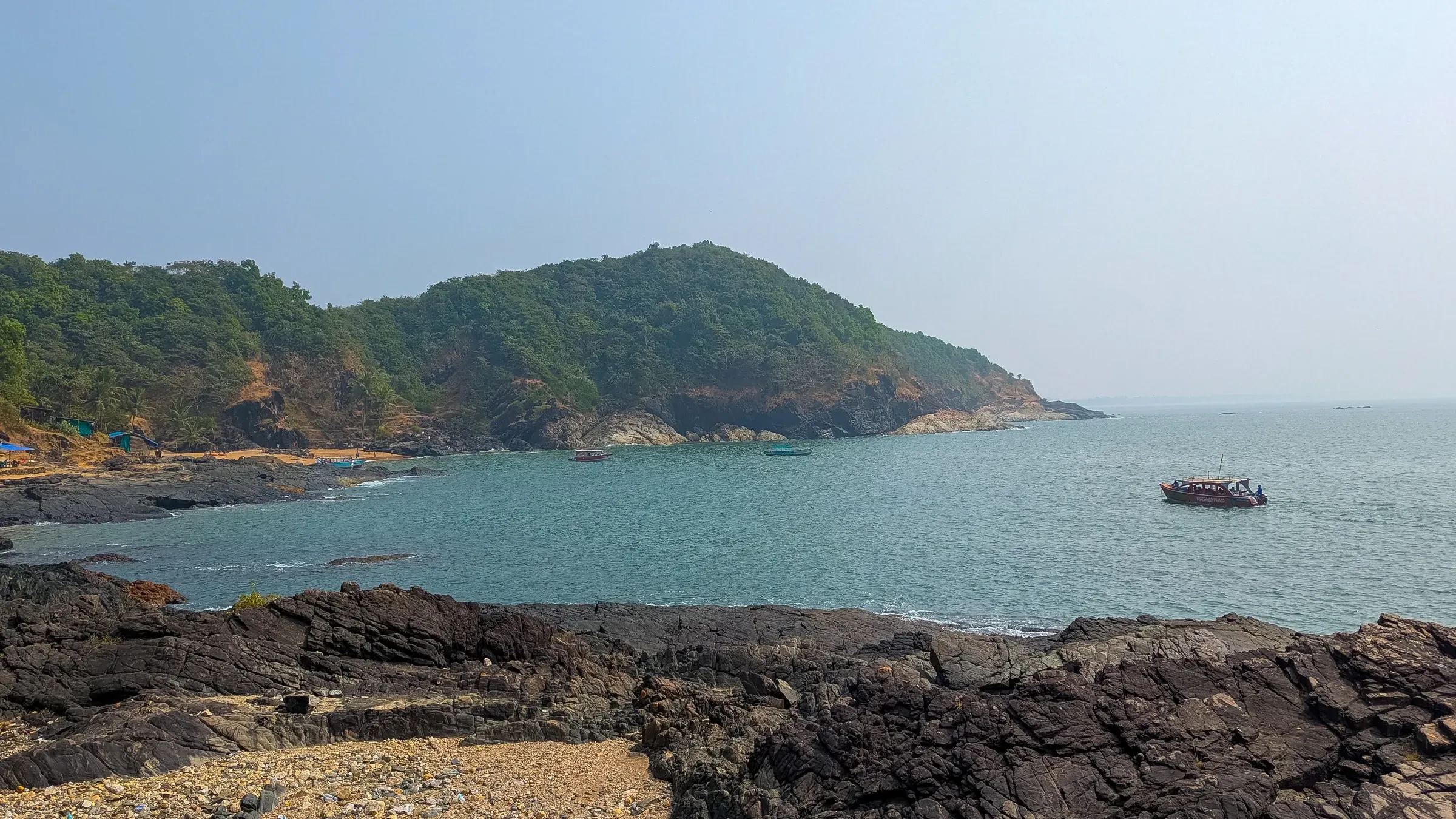 A wooded headland and dark rocks on the coastal trail near Gokarna