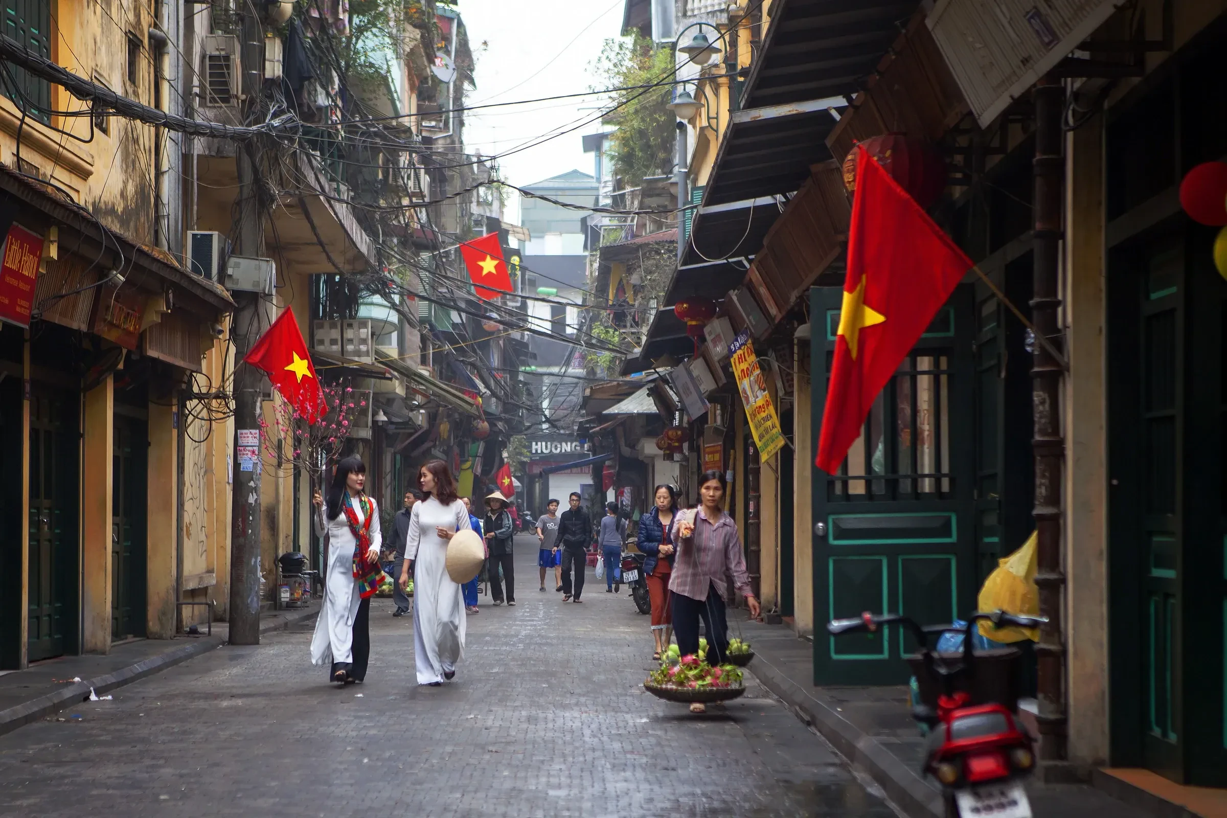Ta Hien Street in Hanoi's Old Quarter, with red flags and people in ao dai walking