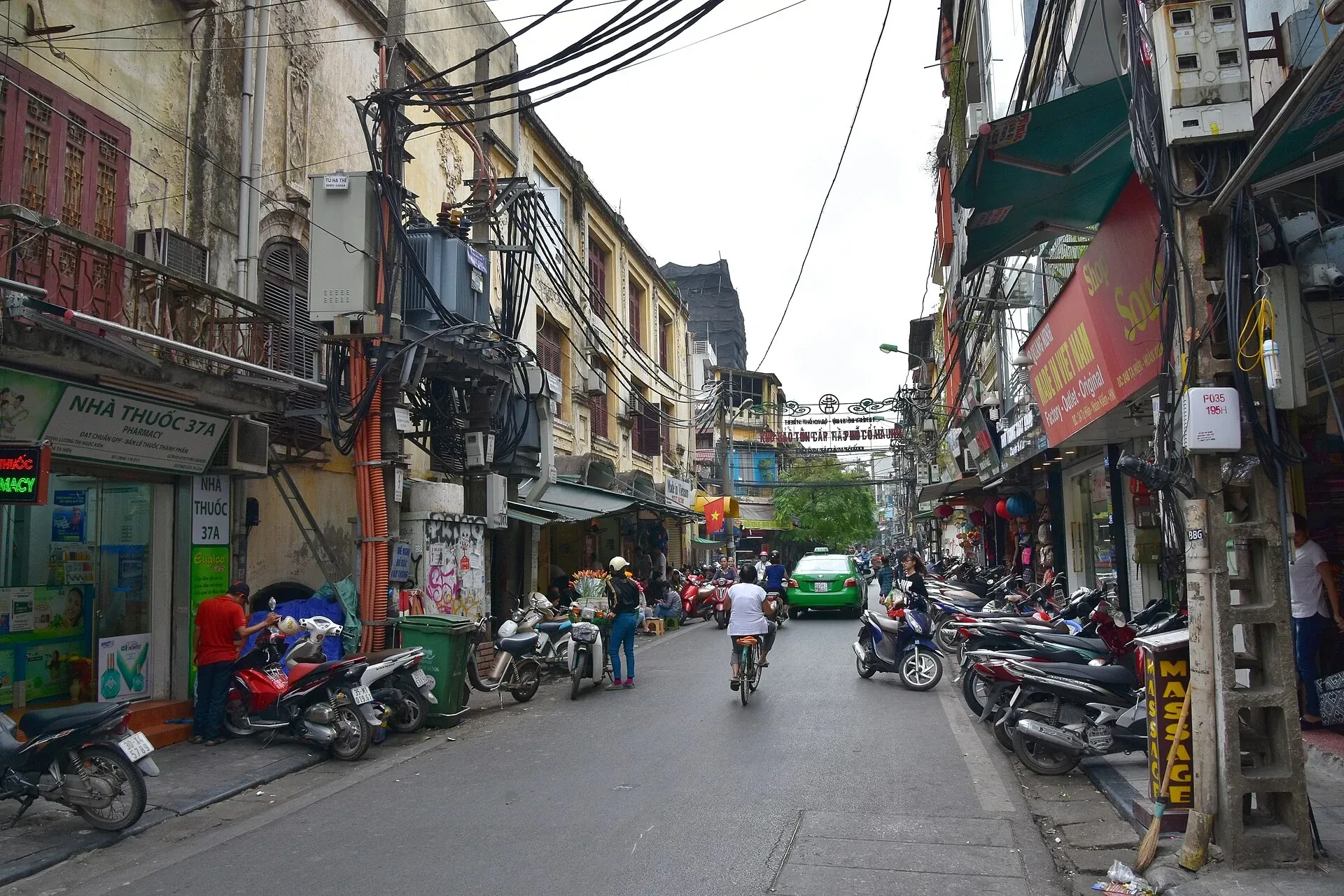 A street in Hanoi's Old Quarter with overhead cables, shopfronts and parked motorbikes