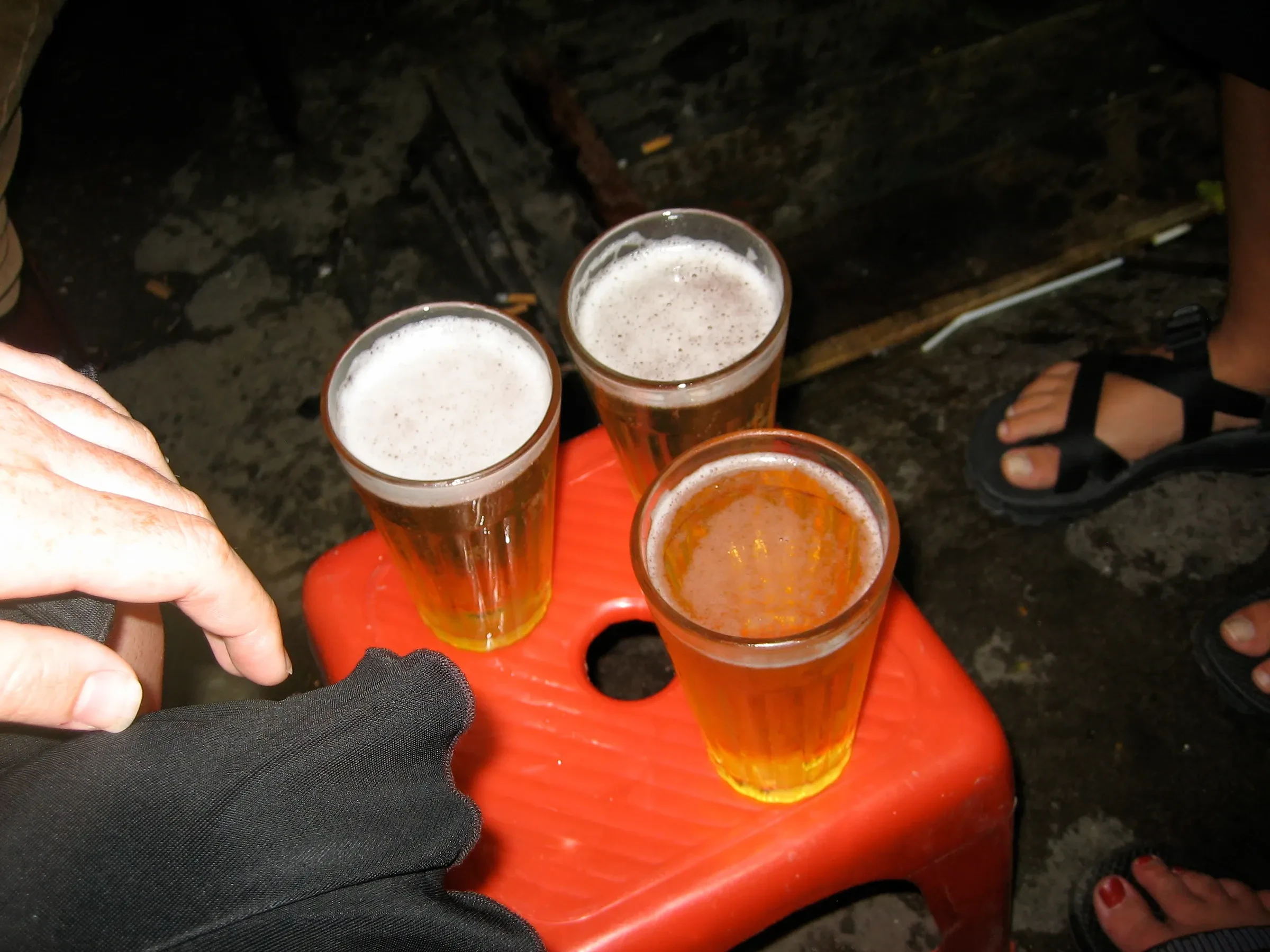 Three glasses of bia hoi on a red plastic stool in Hanoi
