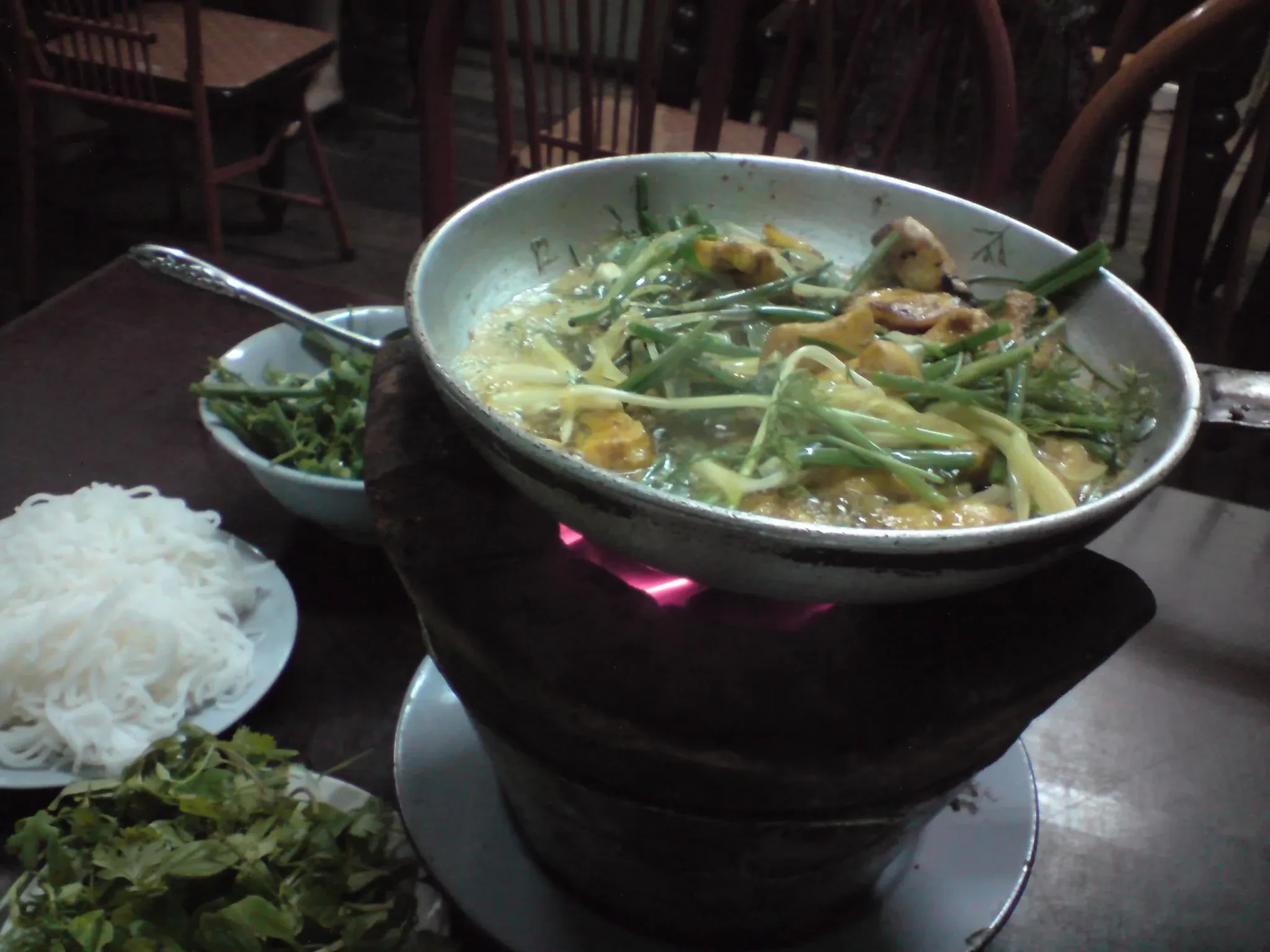 Cha ca fish and herbs cooking in a pan over a small burner at the table in Hanoi