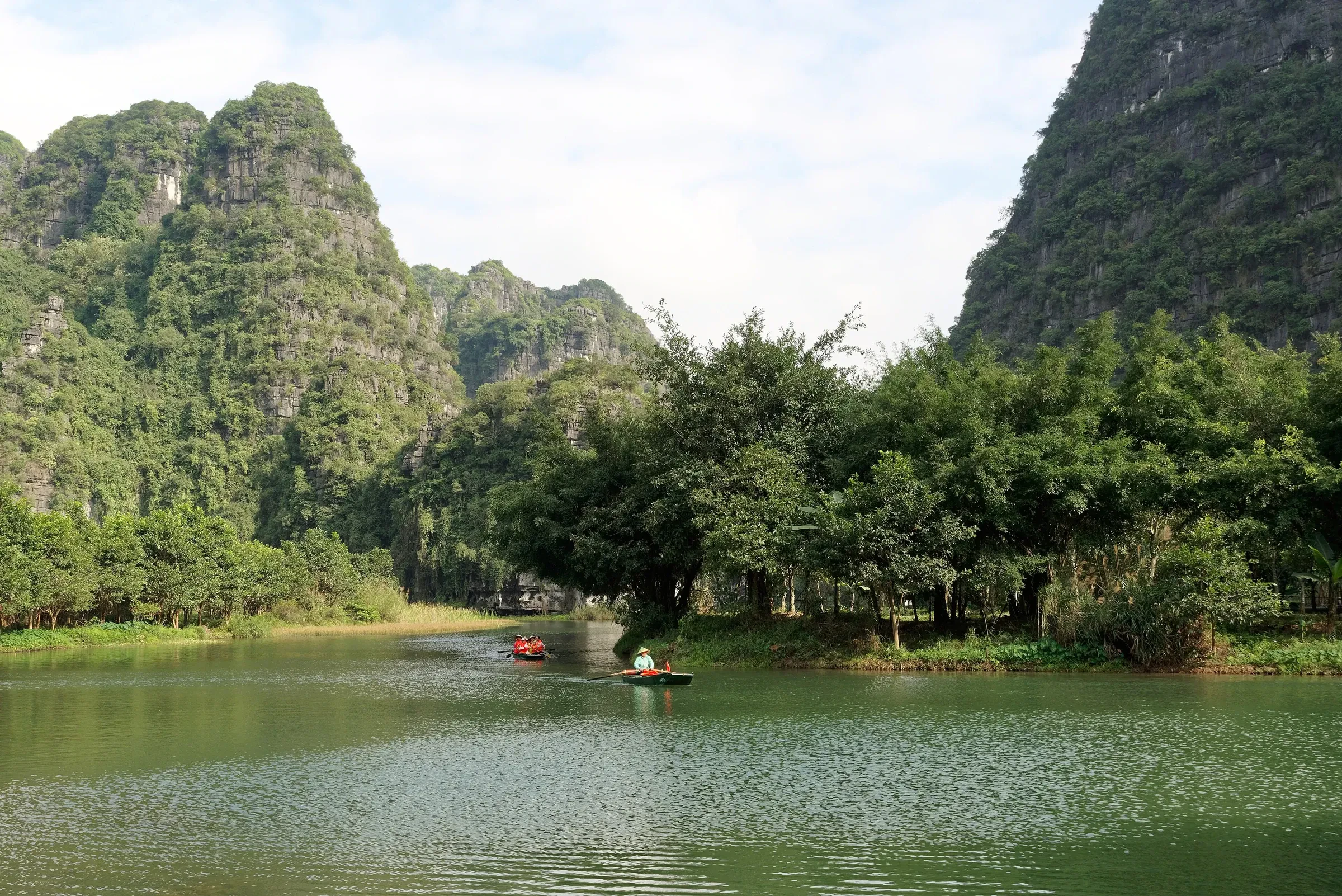 A river lined with limestone karst at Trang An in Ninh Binh, with a small boat in the distance