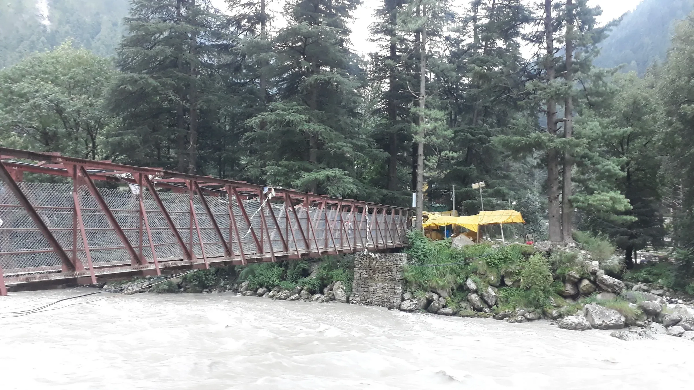 The steel bridge over the Parvati river among pines at Kasol