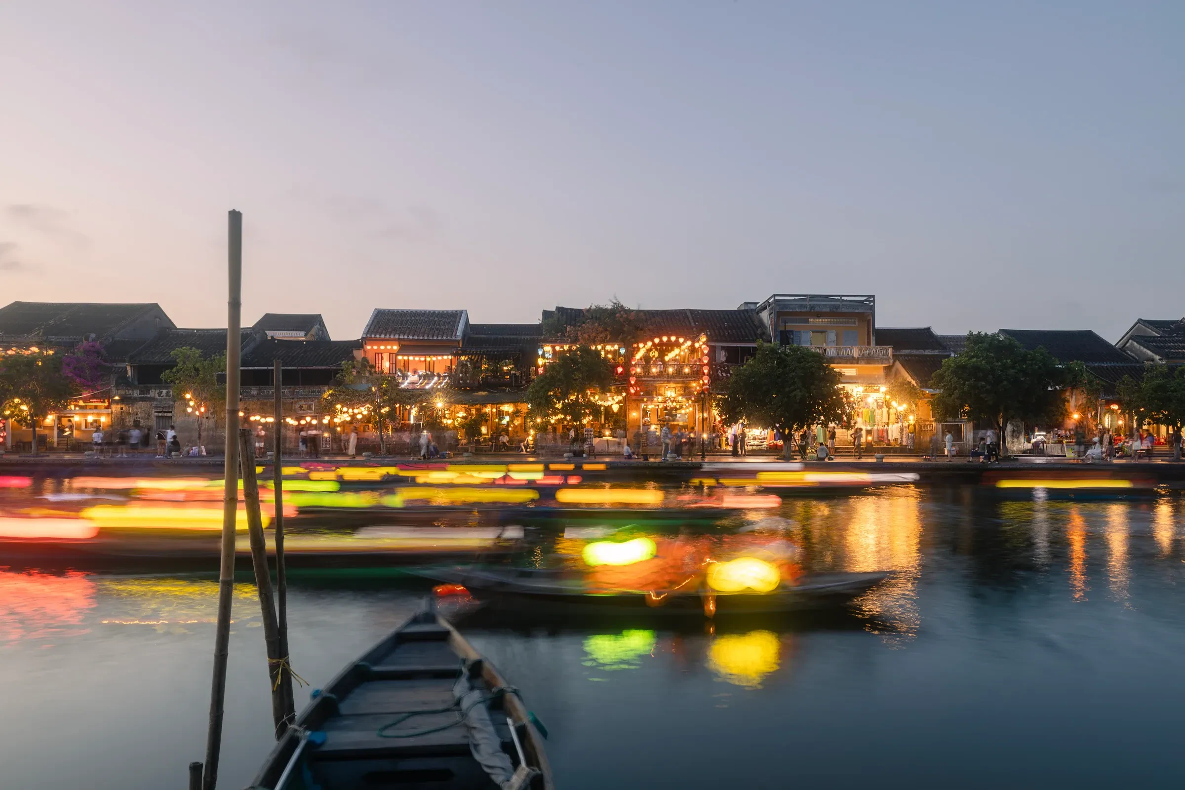 Moored wooden boats and lantern lights along the riverbank in Hoi An at dusk