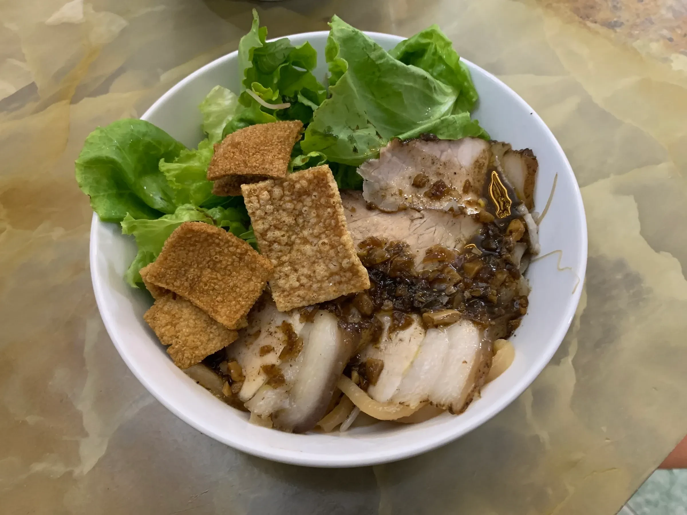 A bowl of cao lau noodles with pork, crackling and herbs in Hoi An