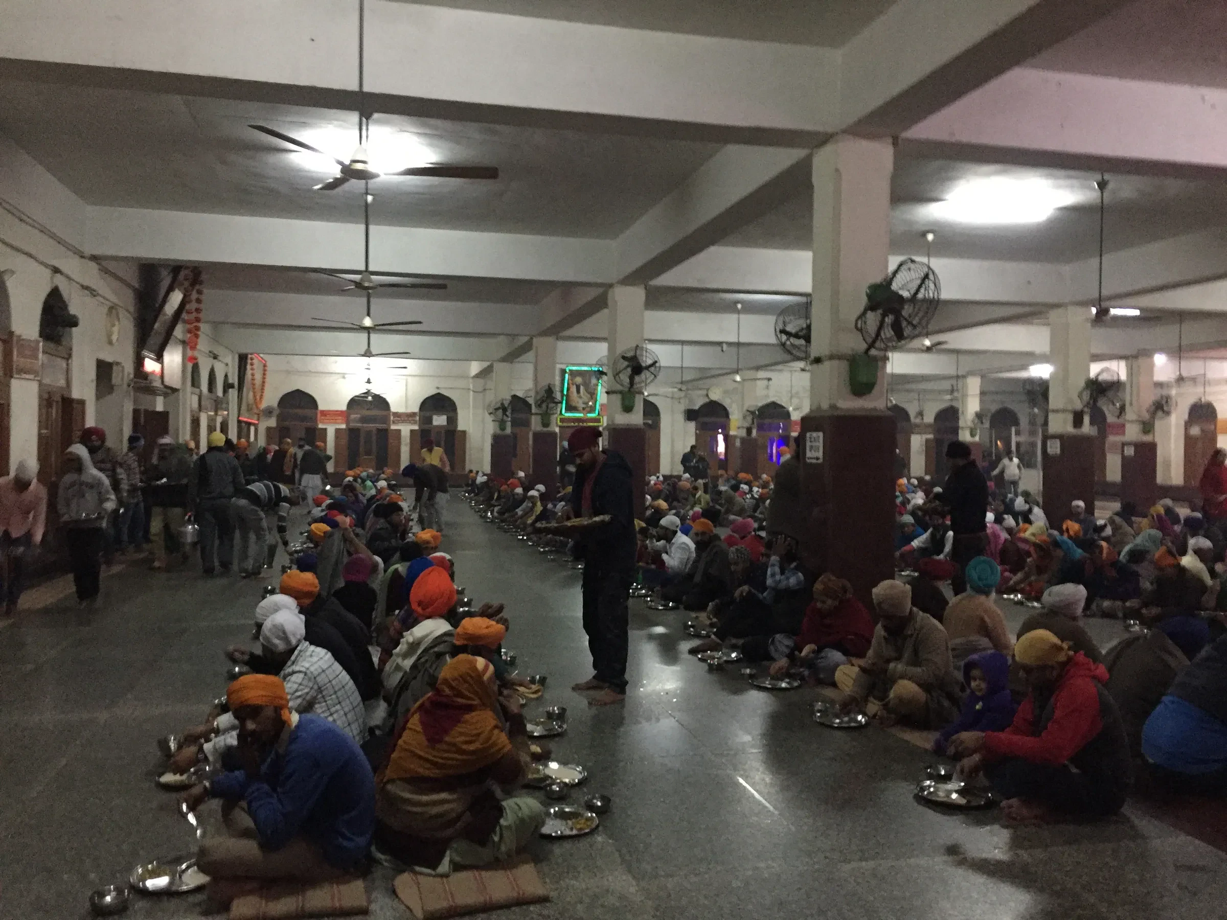 Rows of people sitting on the floor eating in the langar hall at the Golden Temple