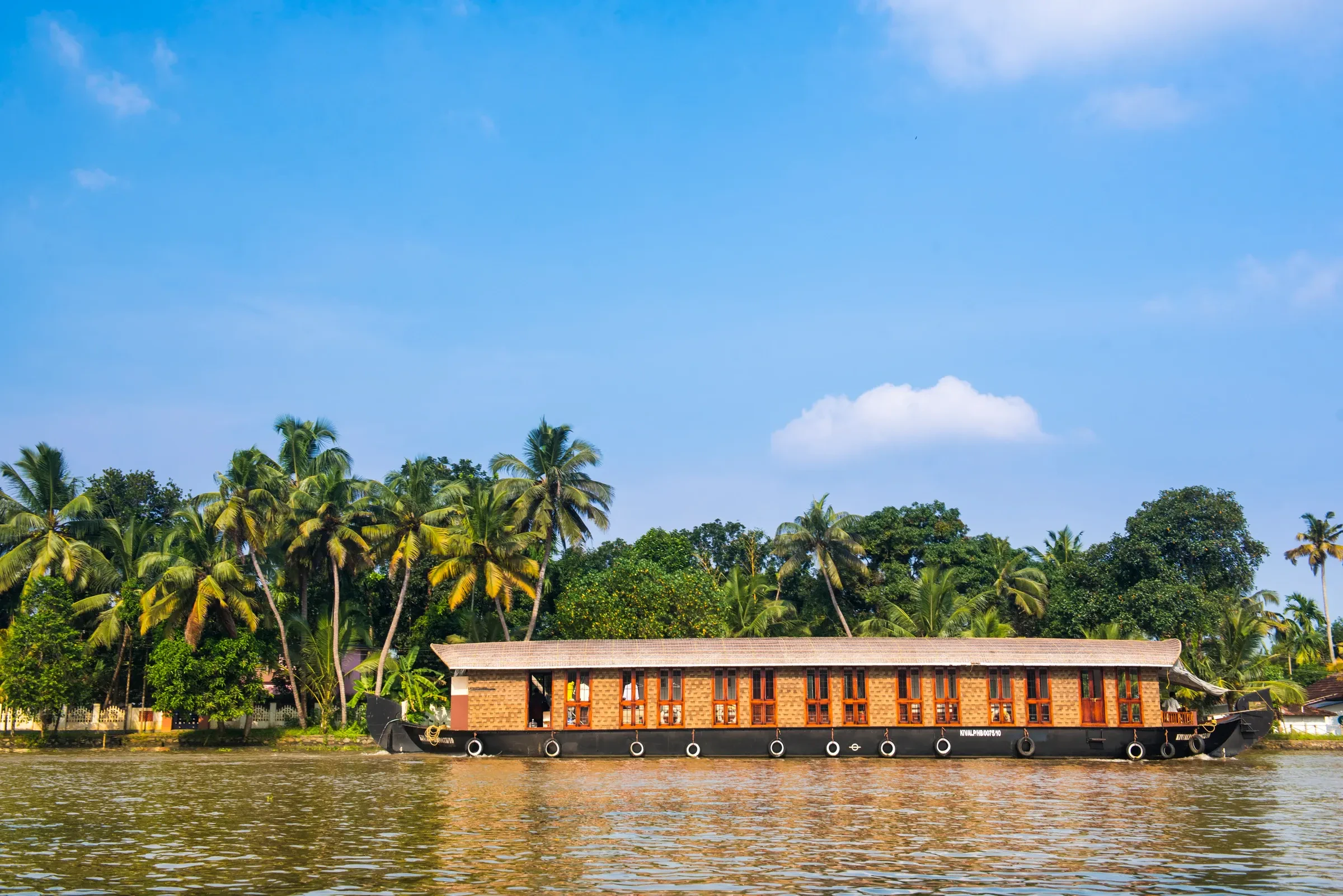 A houseboat moving along the backwaters near Alleppey in Kerala, with palm trees along the bank.