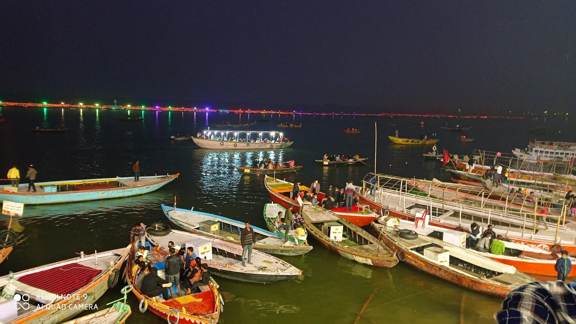 Rowing boats crowded together on the Ganges at night beside the lit ghats of Varanasi