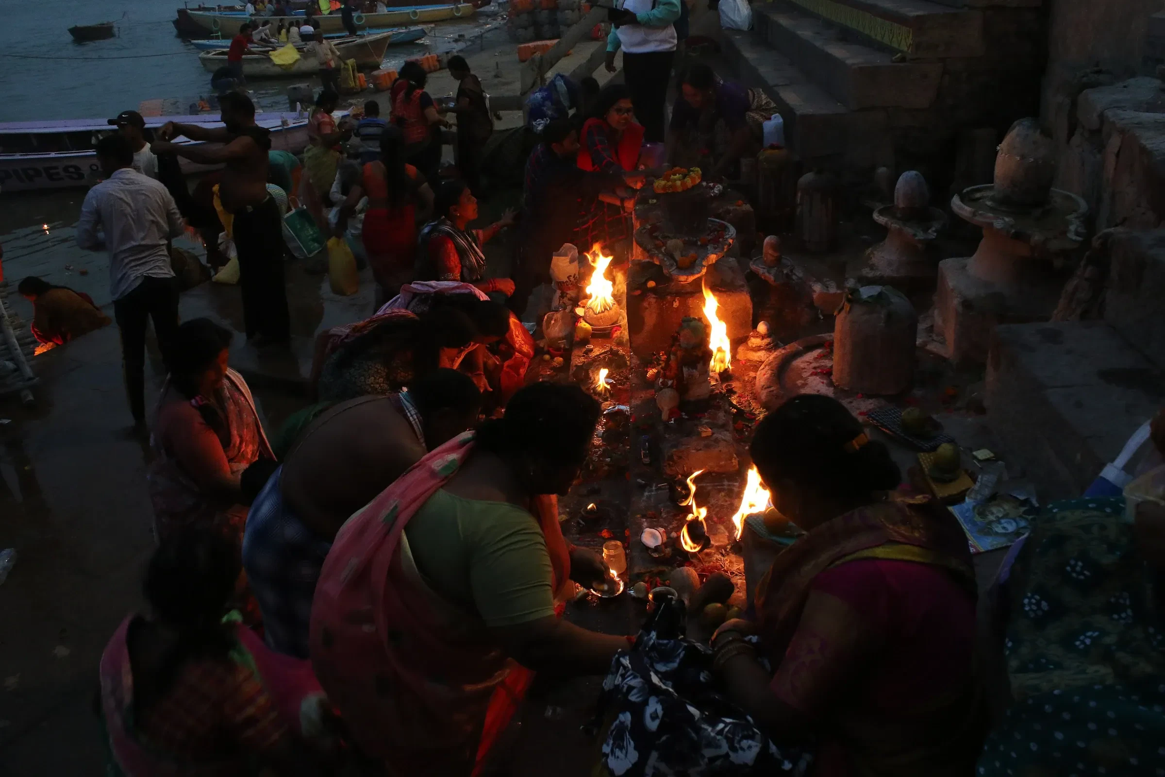 Rows of small flames burning along the red and white steps of a Varanasi ghat as people light lamps before Dev Deepawali