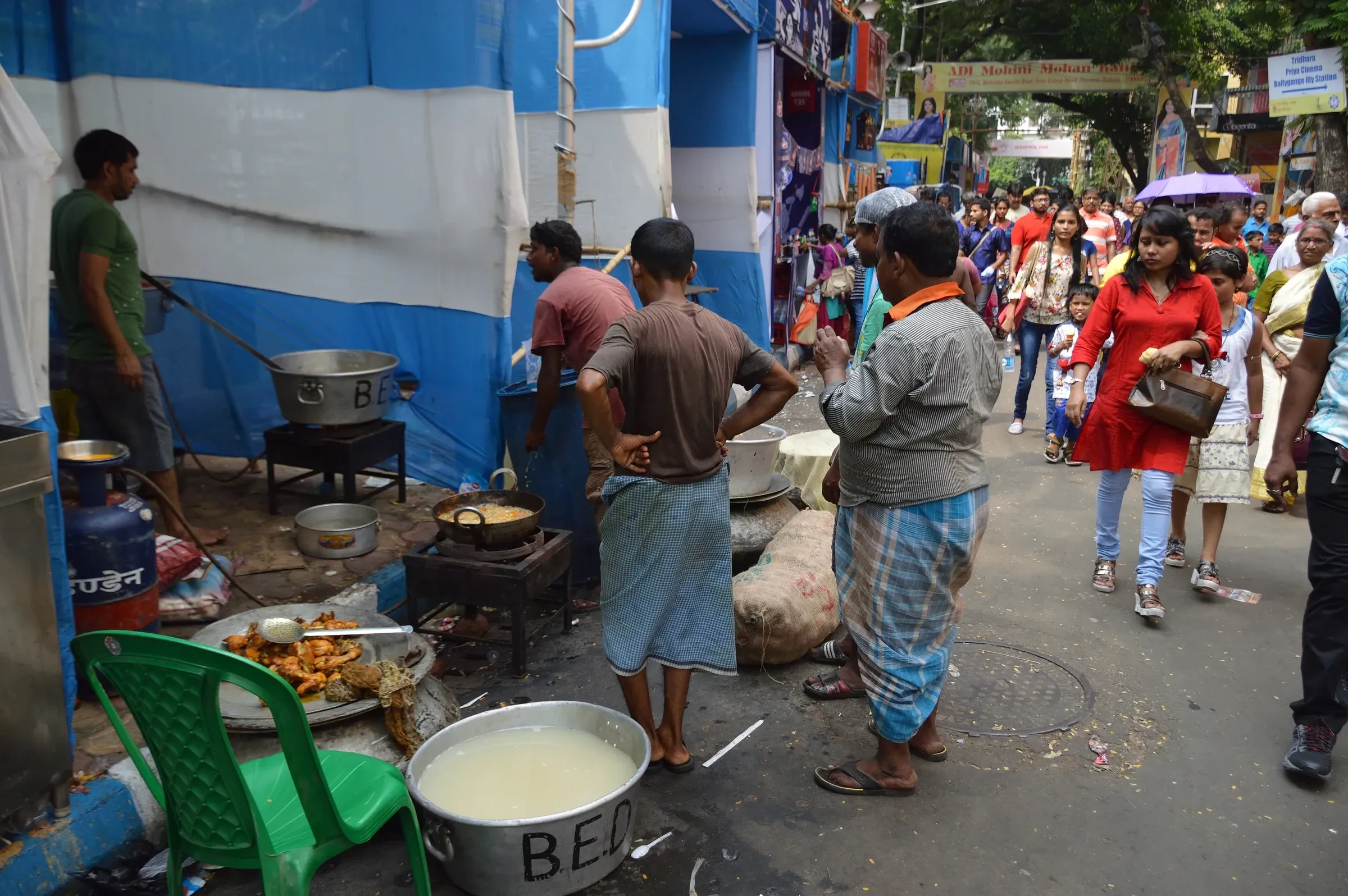 Cooks frying street food at roadside stalls beside a crowded road during Durga Puja in Kolkata